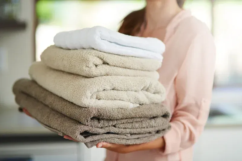 Woman holding a stack of folded towels in varying shades of beige and white.