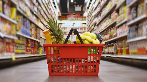 Red shopping basket filled with groceries in a supermarket aisle.