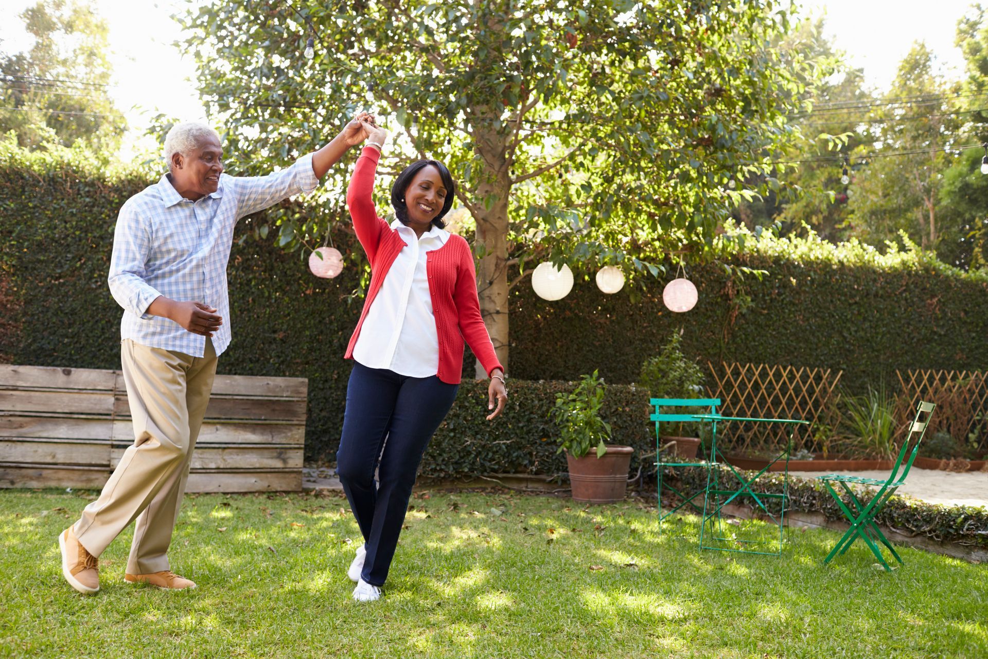 Couple dancing in a sunlit backyard with trees and round paper lanterns.