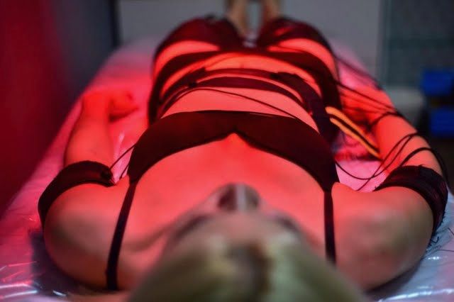 Une femme est allongée sur un lit avec des lumières rouges sur son corps.