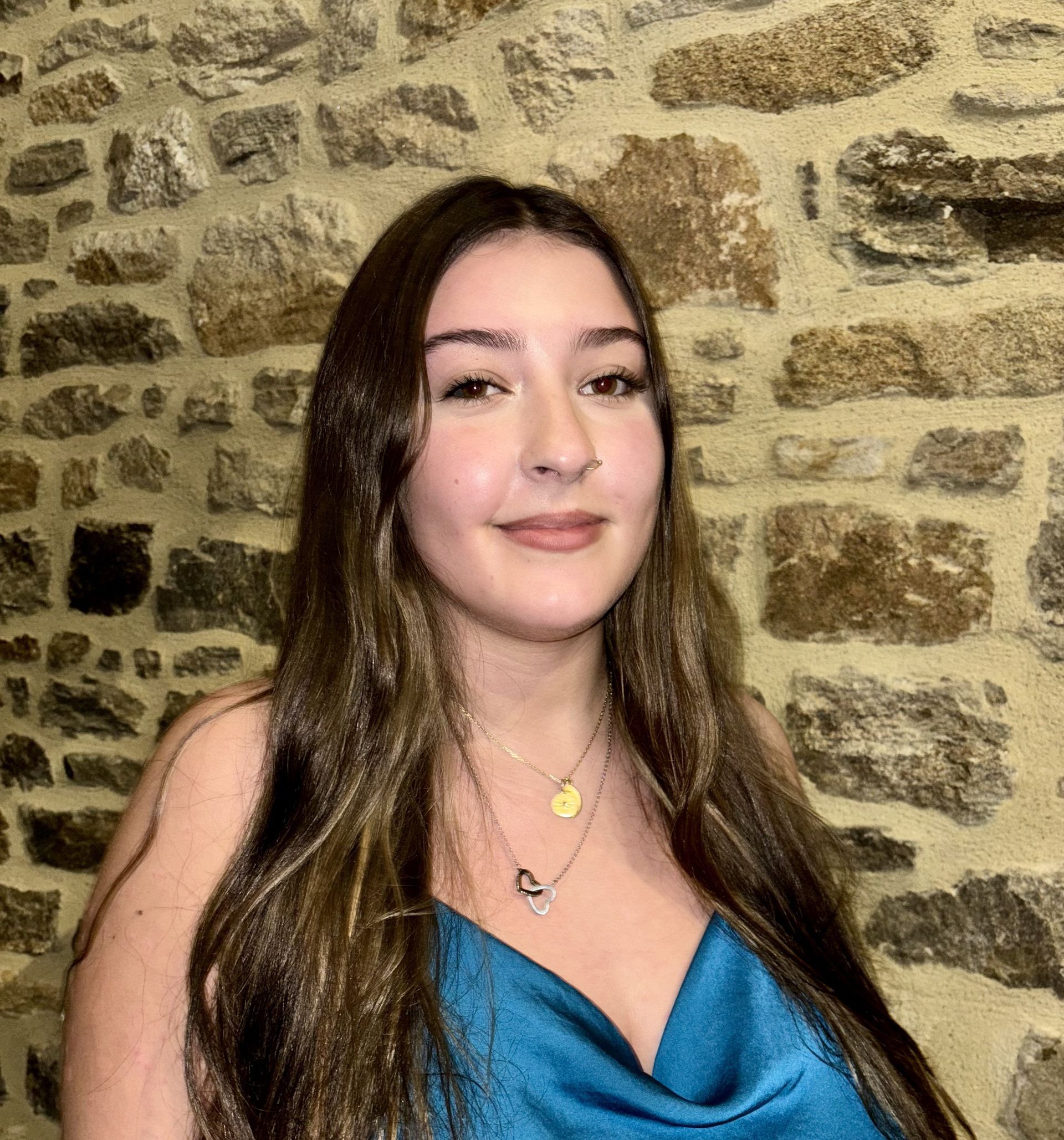 Une femme en robe bleue se tient devant un mur de pierre.