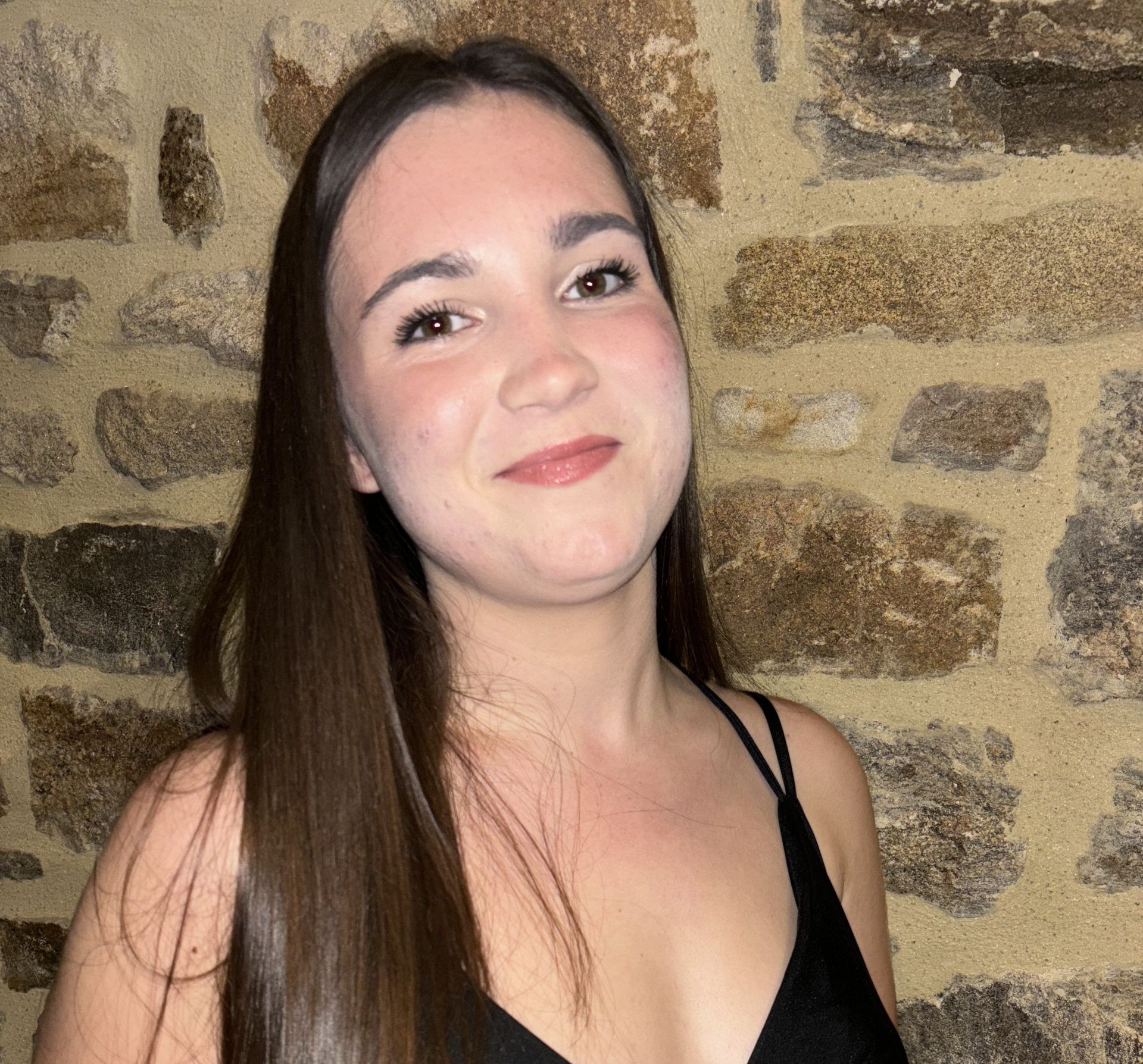 Une femme en haut noir se tient devant un mur de pierre.