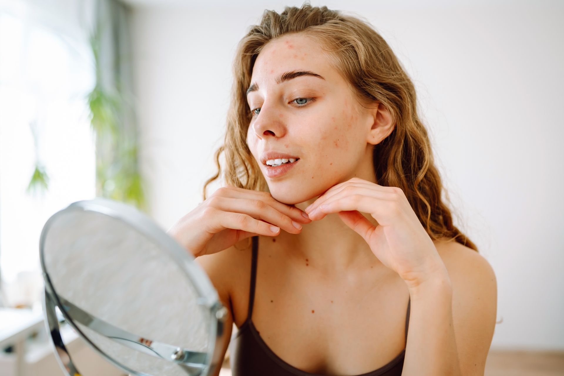 A woman is looking at her face in a mirror.