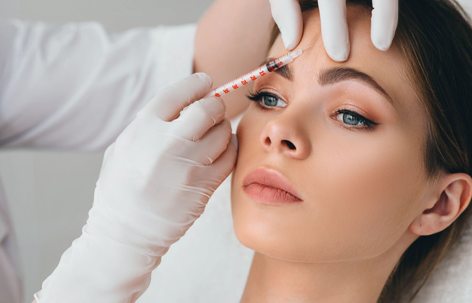 A woman is getting a botox injection in her forehead.