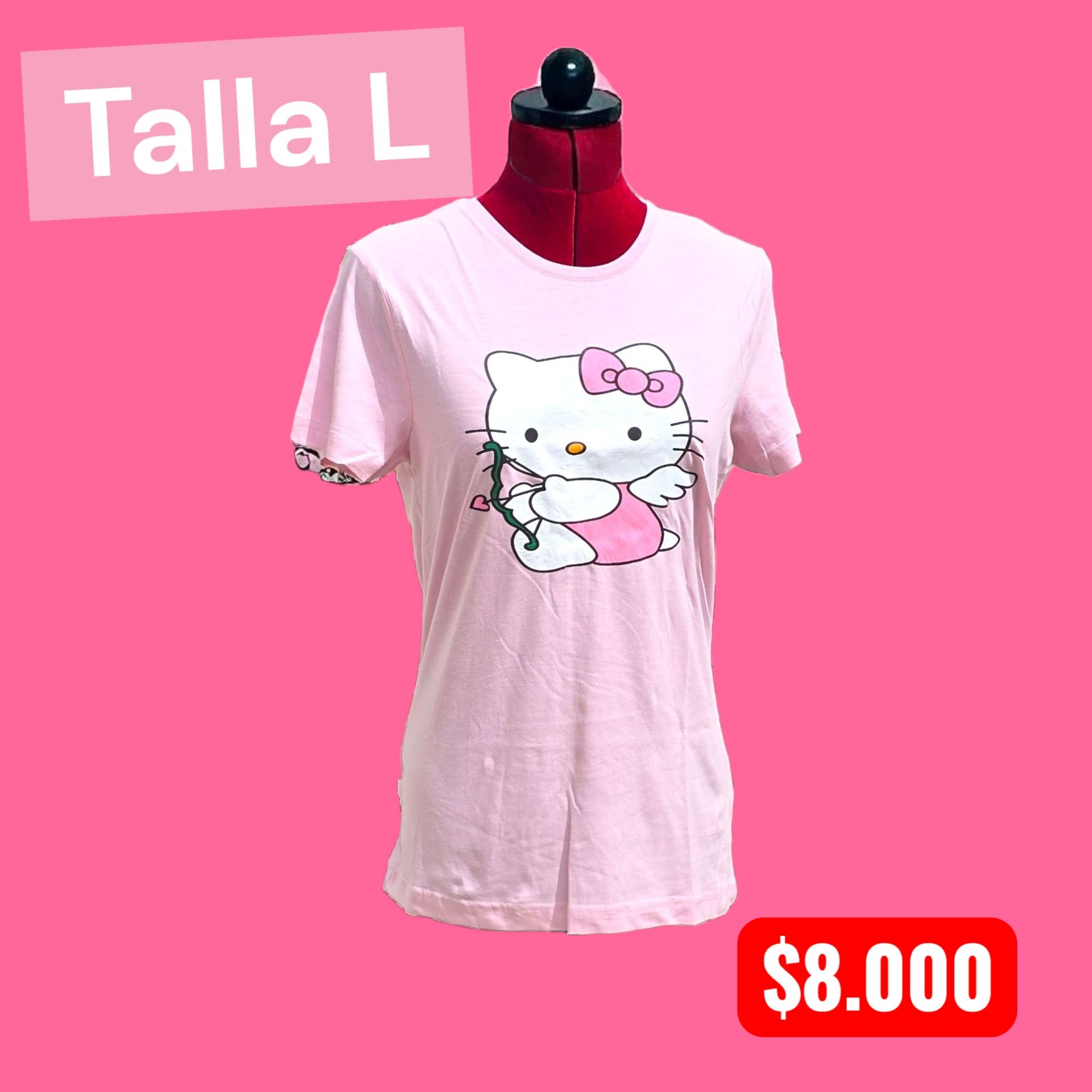 Una mujer rapada, con una polera rosa de Hello Kitty y vaqueros negros rotos, está de pie en una habitación con una mesa.