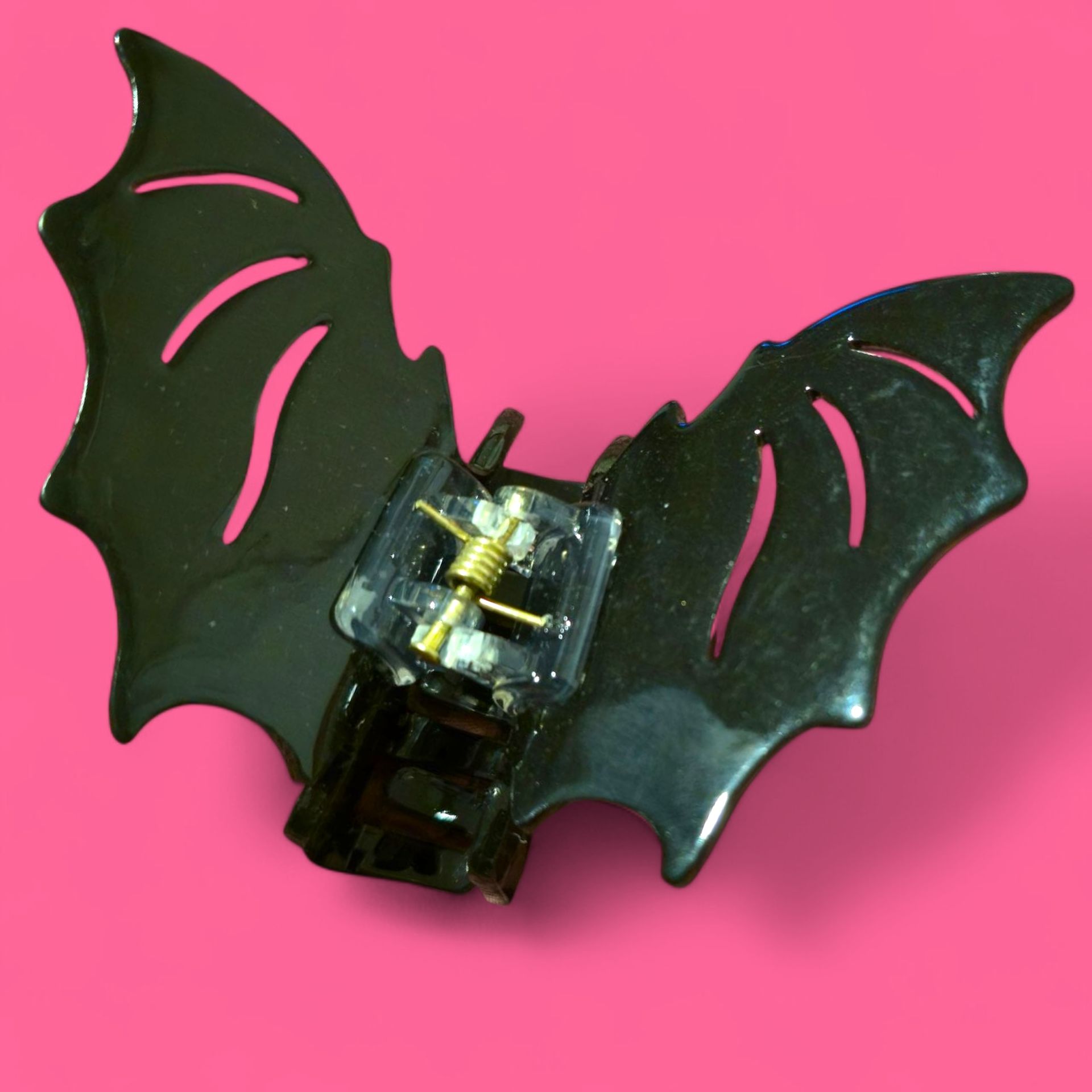 Pinza para el pelo con forma de ala de murciélago negra sobre fondo rosa.