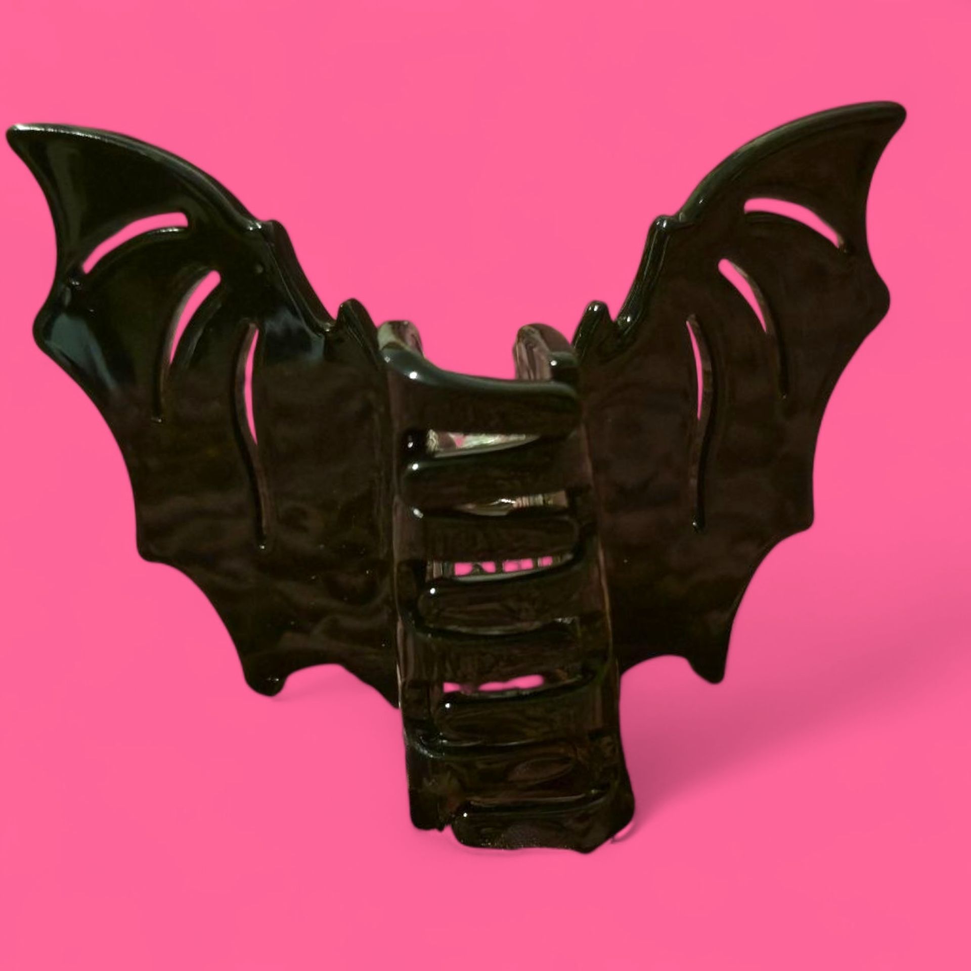 Pinza para el pelo con forma de ala de murciélago negra sobre fondo rosa.