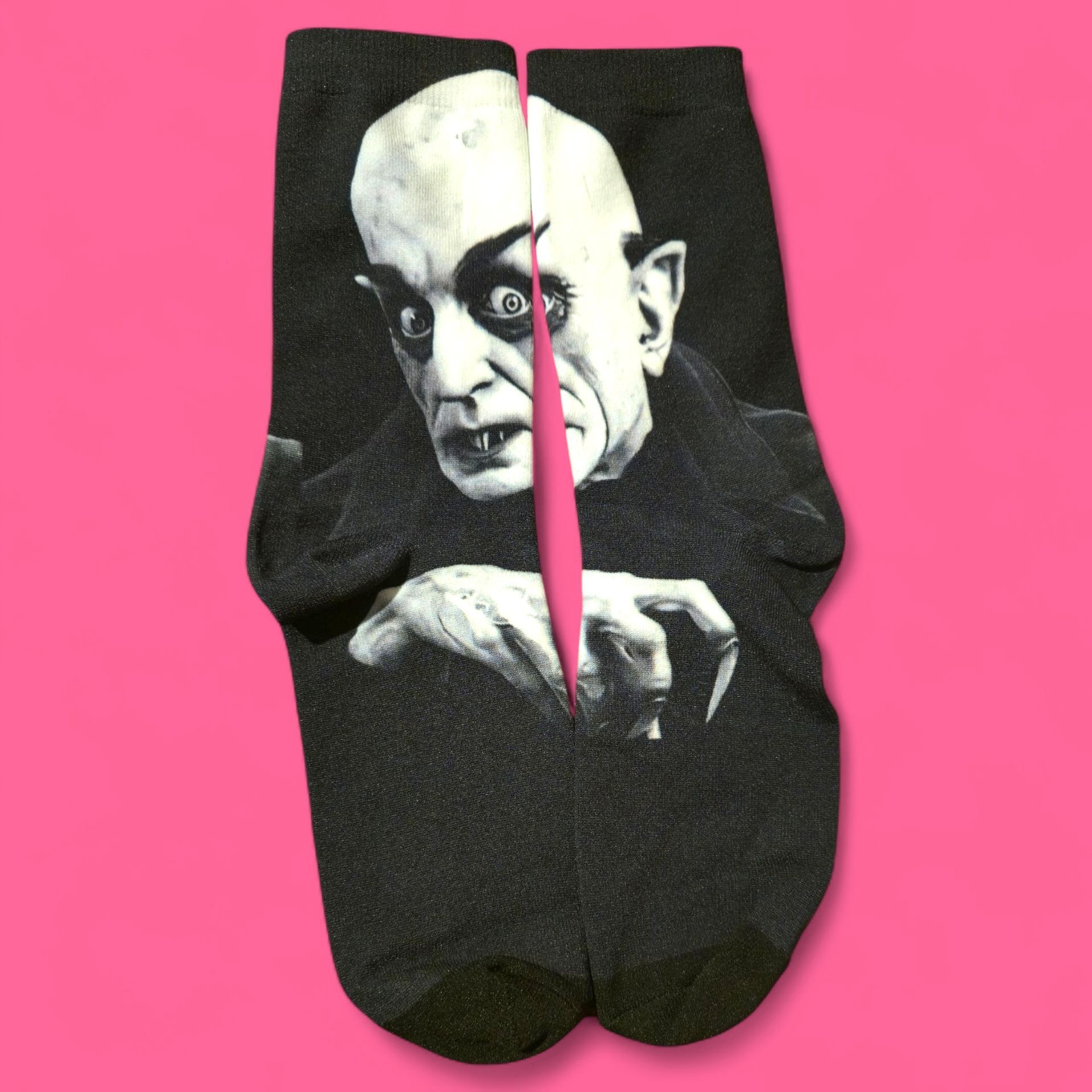 Par de calcetines negros con la imagen de un vampiro calvo sobre fondo rosa.