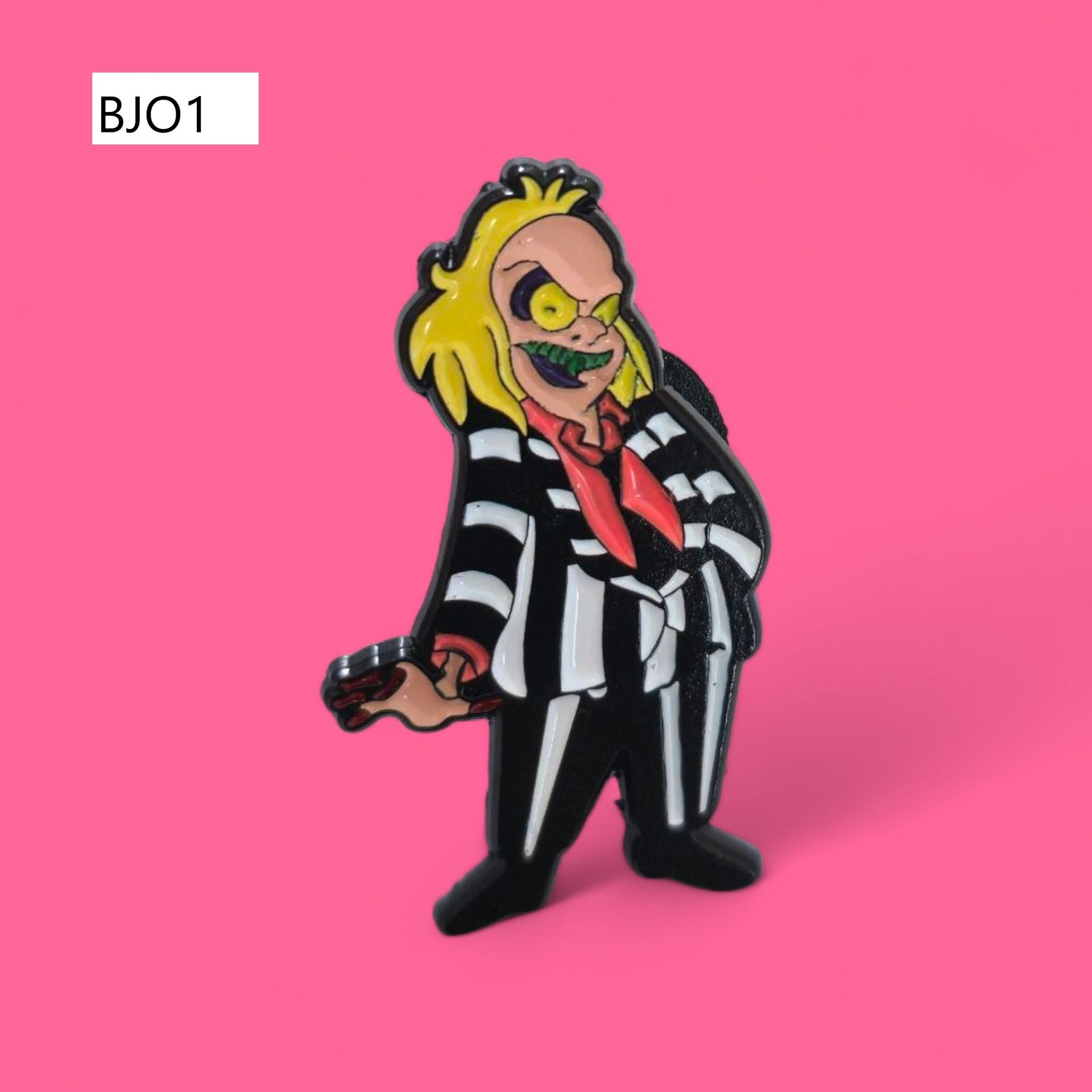 Pin de esmalte de Beetlejuice sobre fondo rosa, con traje de rayas, cabello amarillo y dientes verdes.
