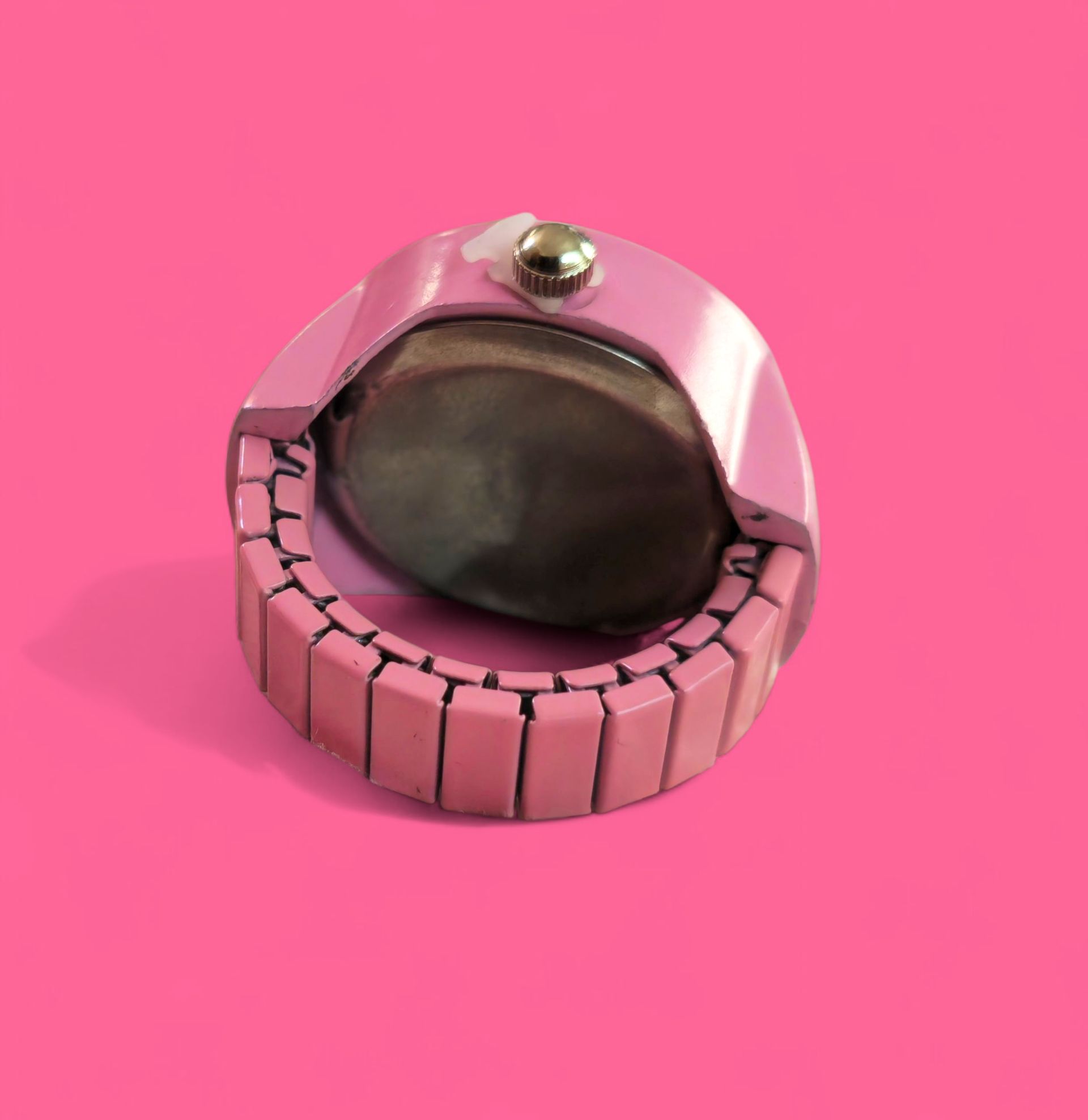 Reloj de pulsera tipo anillo Hello Kitty rosa con bisel con incrustaciones de joyas sobre fondo rosa.