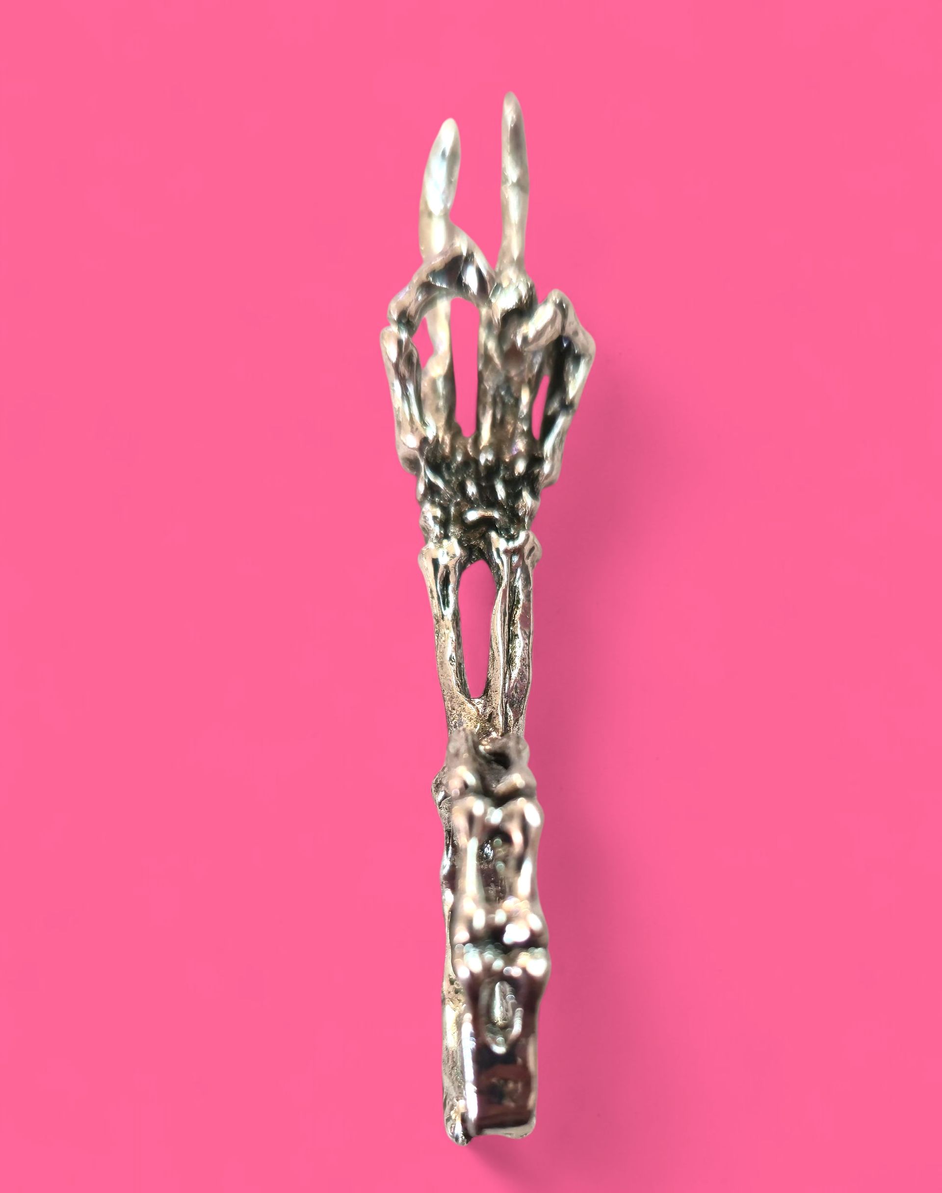 Colgante de mano de esqueleto haciendo el símbolo de la paz, plateado sobre fondo rosa.