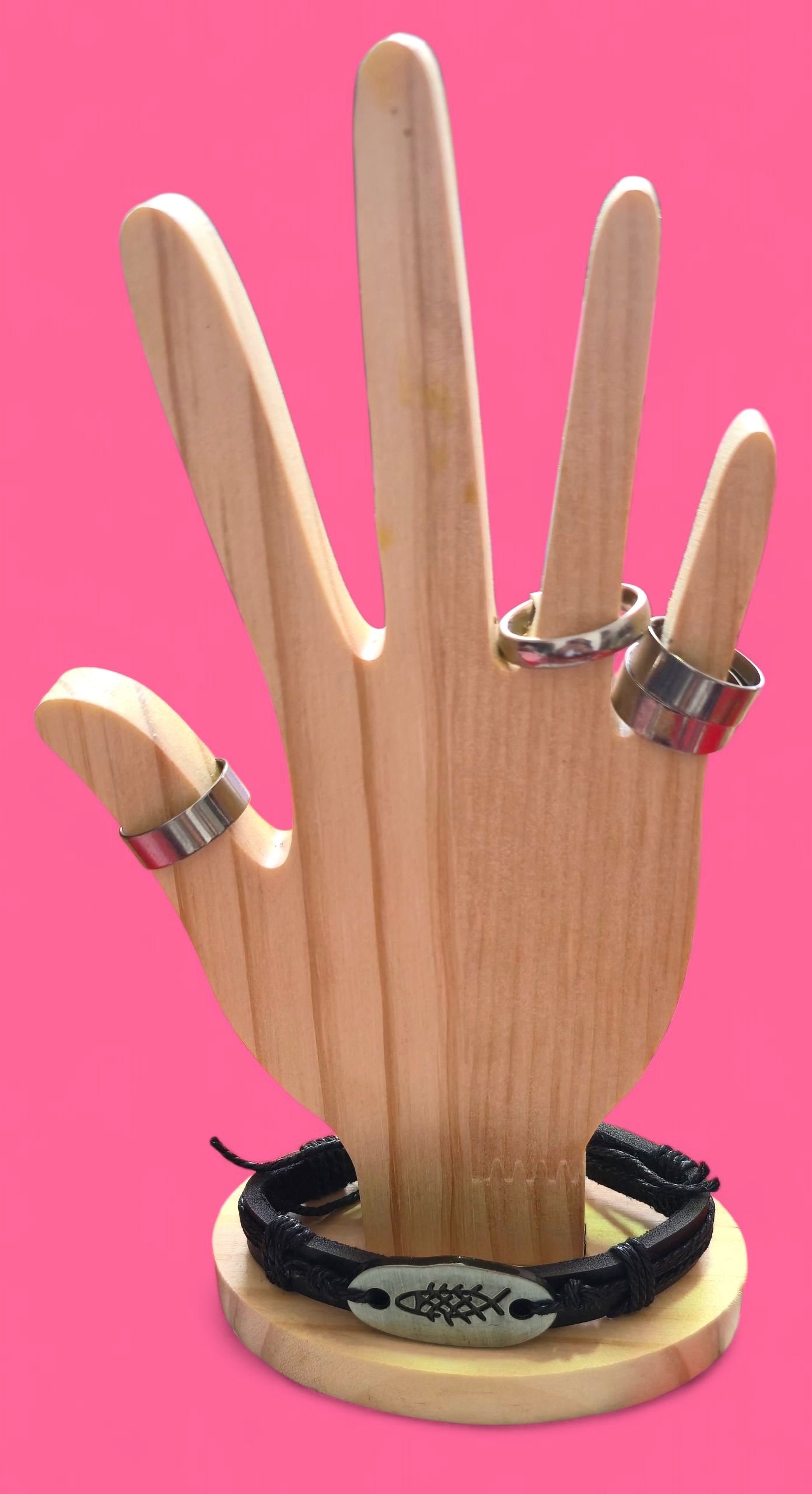 Expositor de anillos en forma de mano de madera con anillos y pulsera sobre fondo rosa.