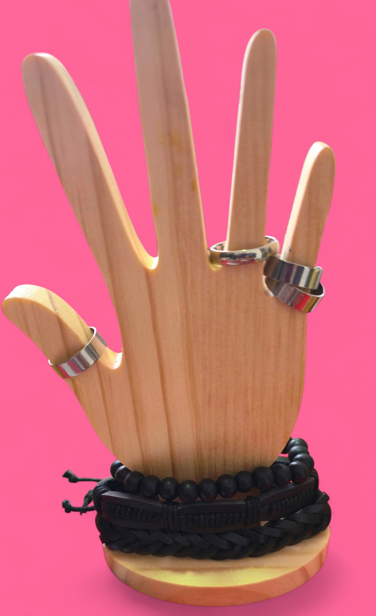 Expositor de joyas en forma de mano de madera con anillos y pulseras negras sobre fondo rosa.