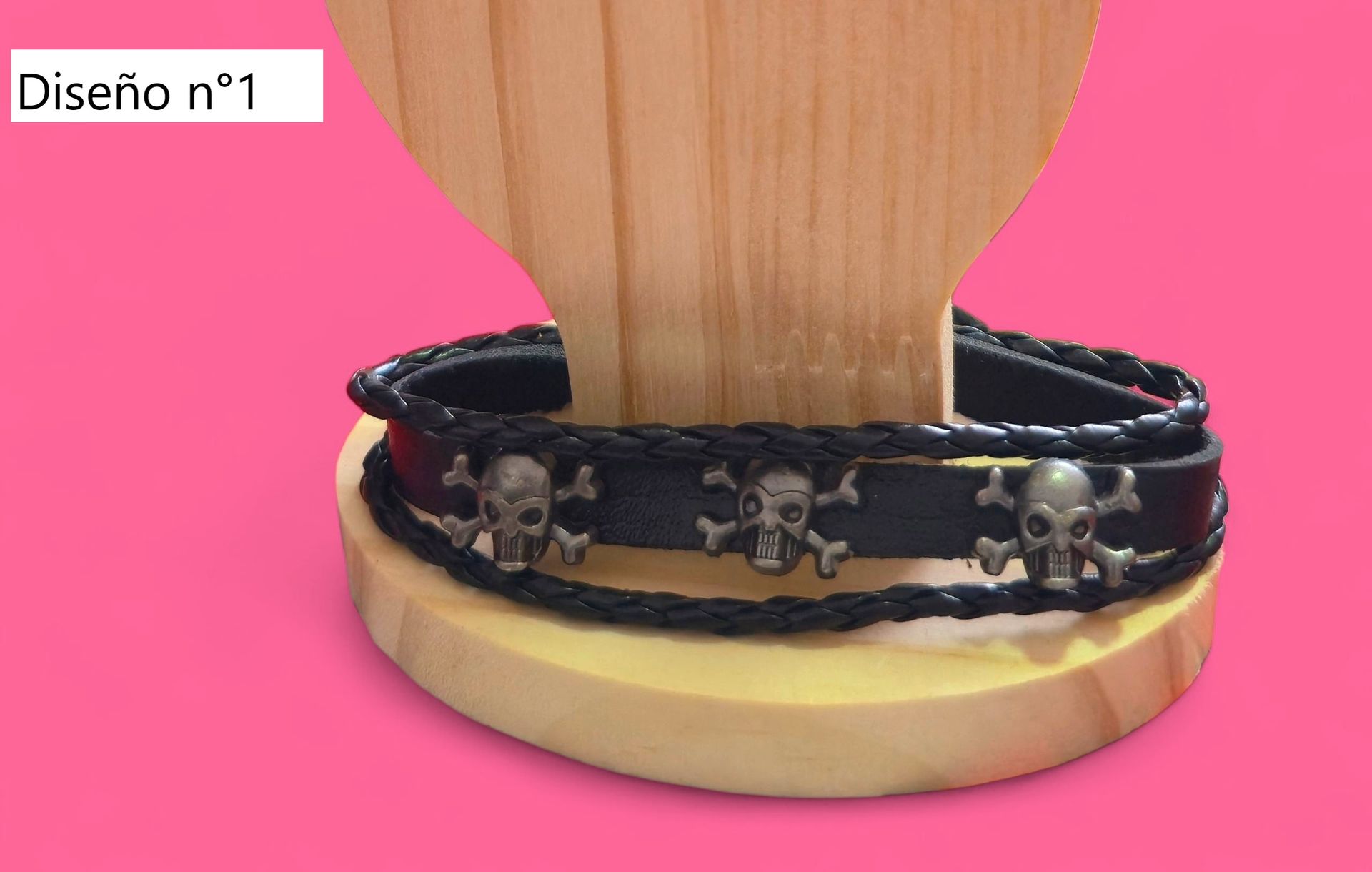 Expositor de joyas de madera en forma de mano con anillos en los dedos y pulseras en la base, sobre un fondo rosa.