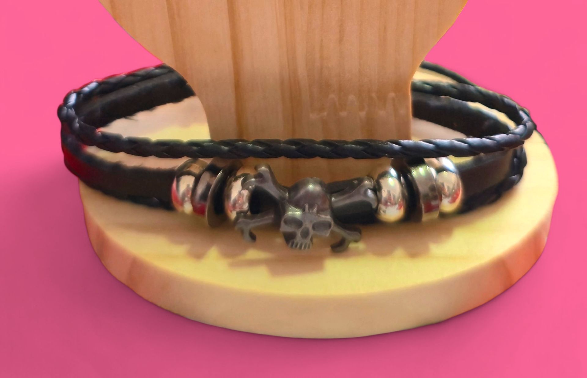 Pulsera de cuero negro con dije de calavera sobre expositor de madera.