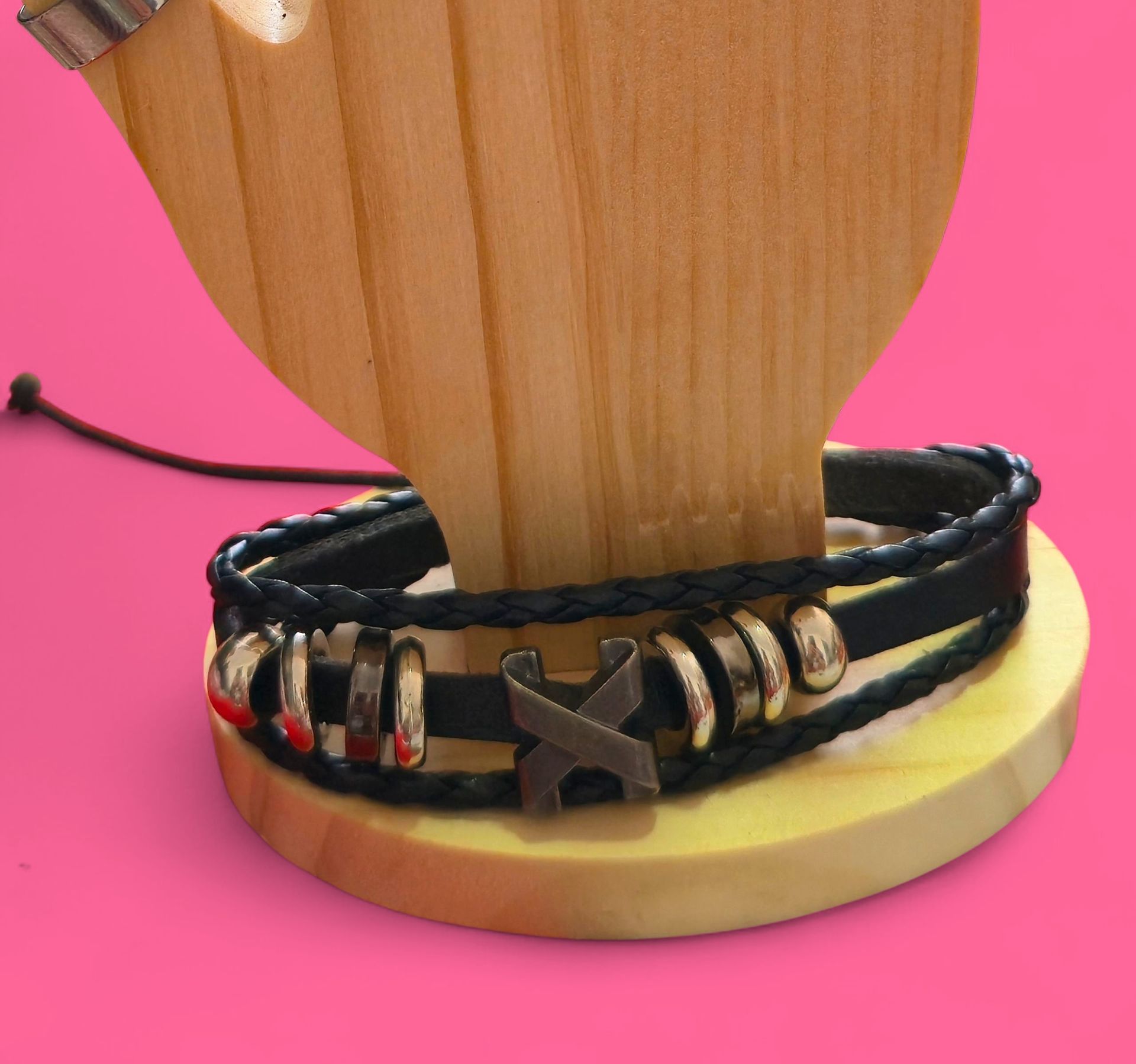 Pulsera de cuero negro con detalles de metal exhibida sobre un soporte de madera sobre un fondo rosa.