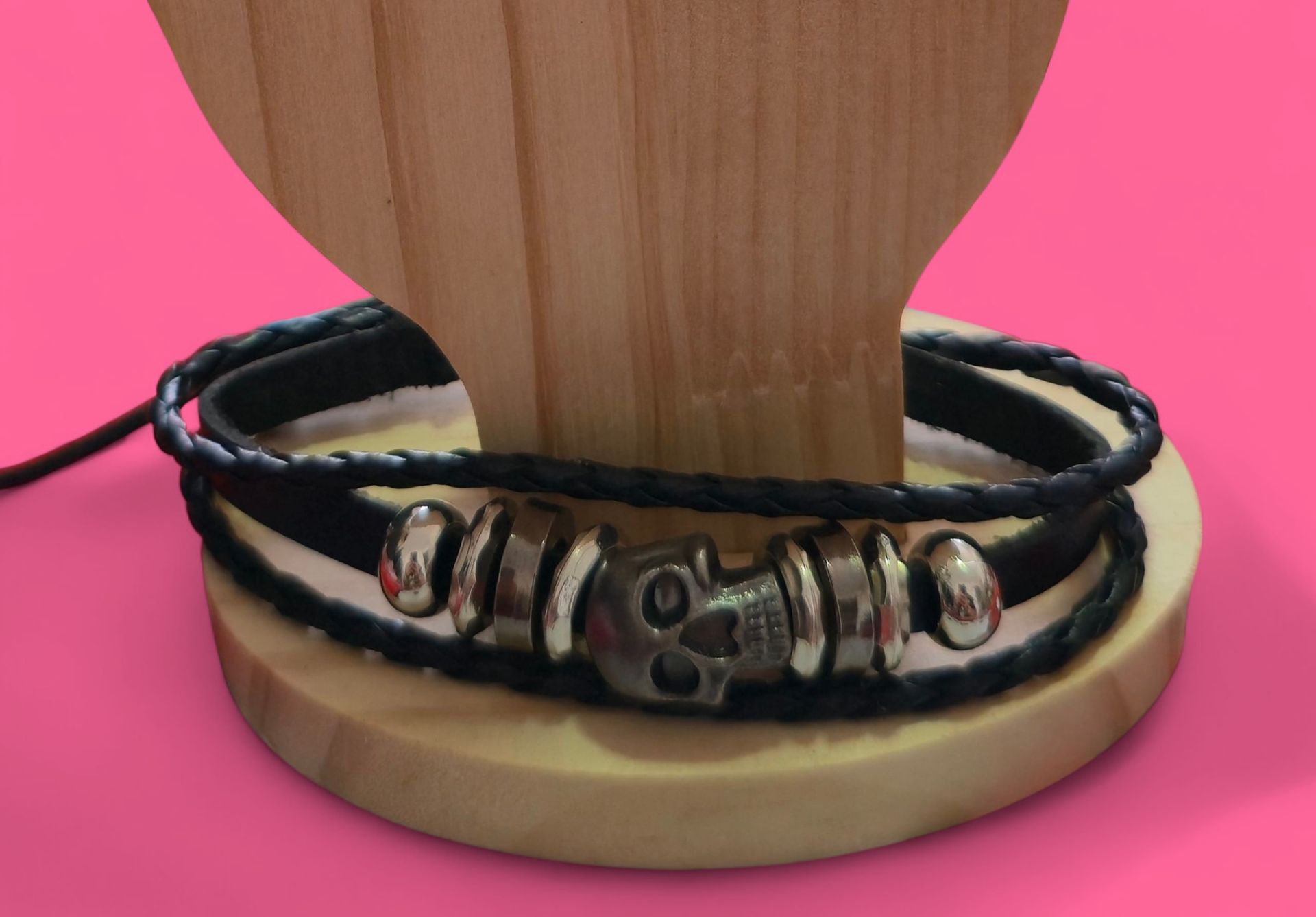 Pulsera de cuero negro con dije de calavera plateada sobre soporte de exhibición de madera.