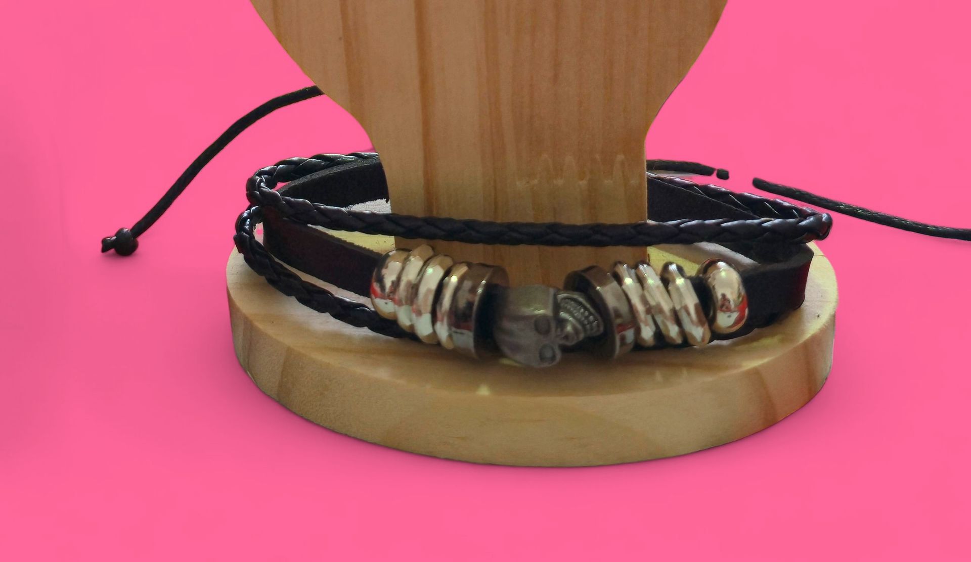 Pulsera de cuero negro con detalles plateados sobre un soporte de madera sobre un fondo rosa.