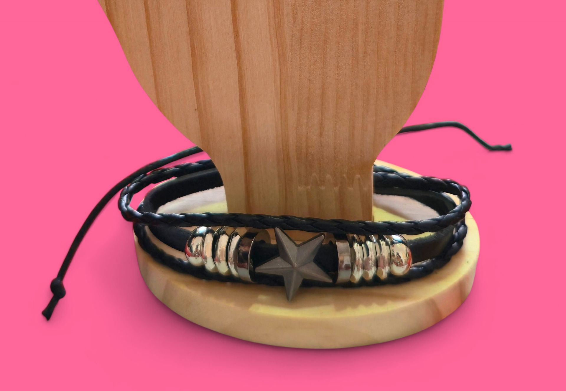 Pulsera de cuero negro con detalles plateados y una estrella sobre soporte de madera.
