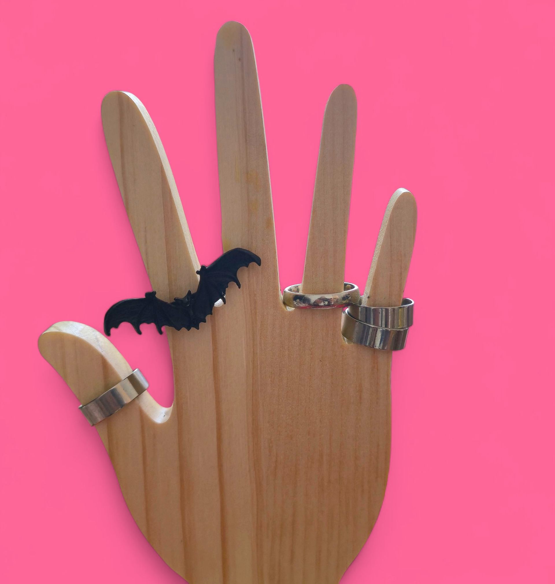 Anillo de murciélago negro sobre un soporte de madera contra un fondo rosa.