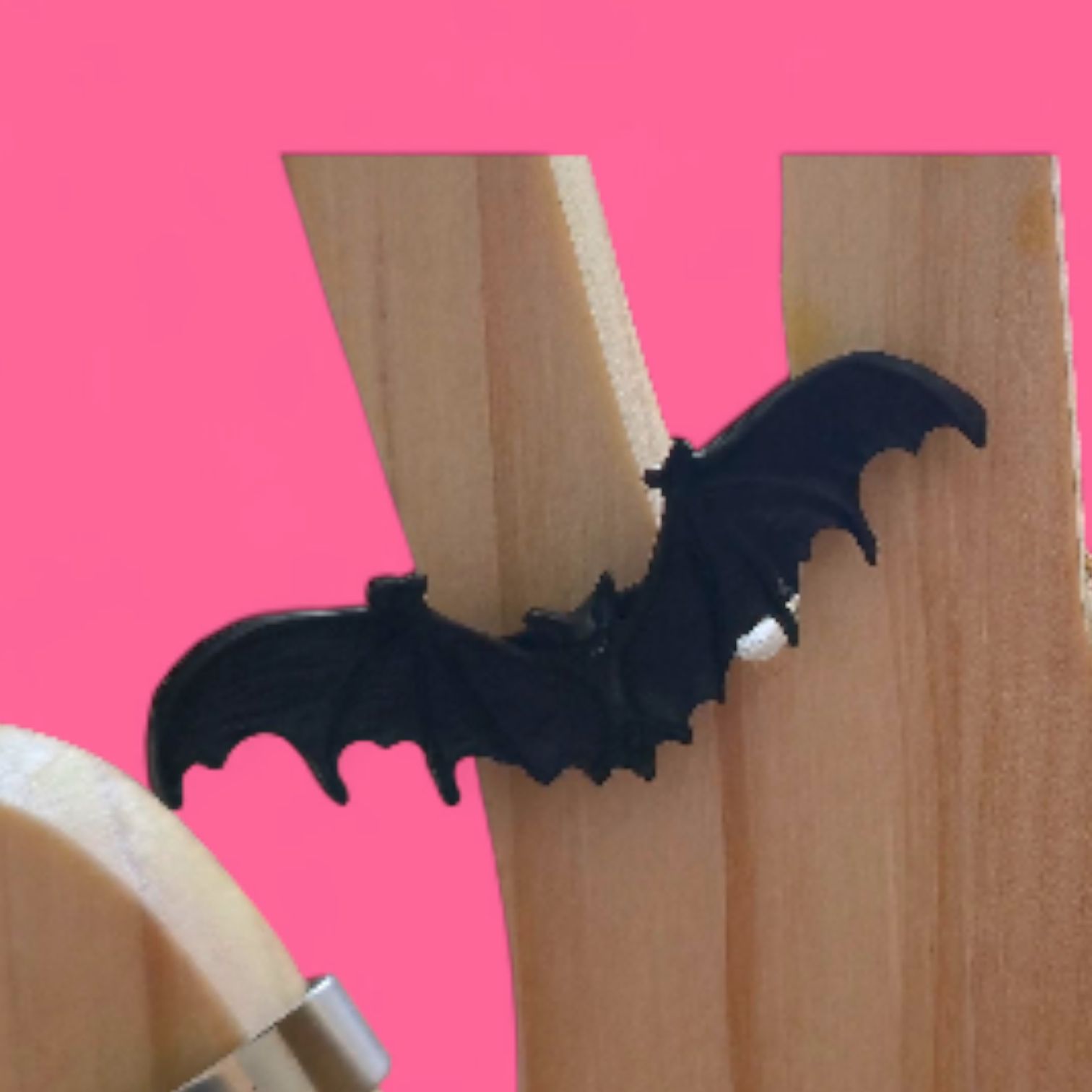 Anillo de murciélago negro sobre un soporte de madera contra un fondo rosa.