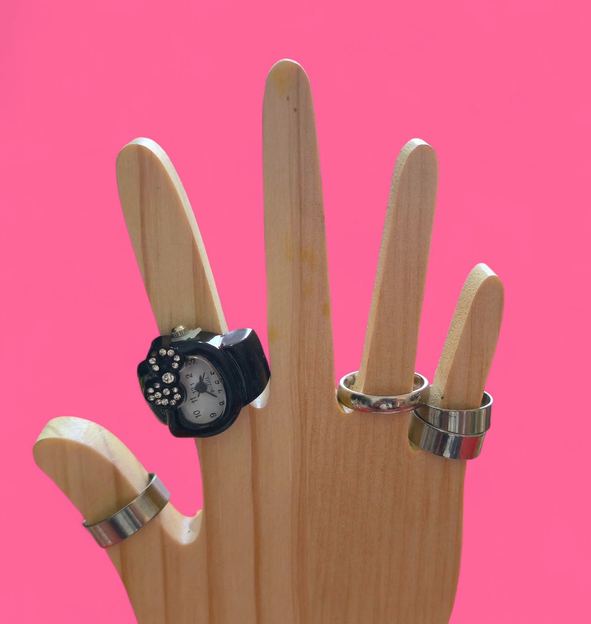 Soporte de anillos de madera con forma de mano, con un anillo de reloj negro y un anillo de banda plateado
