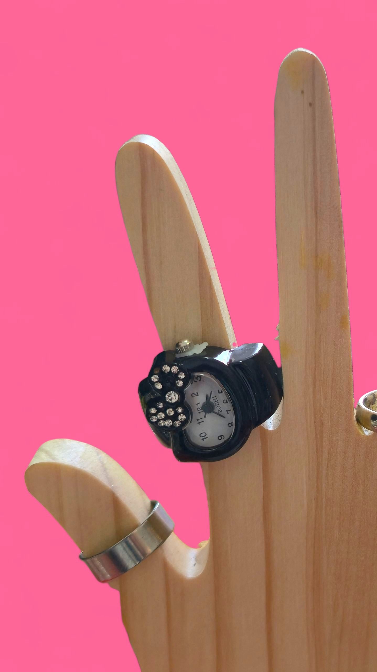 Soporte de anillos de madera con forma de mano, con un anillo de reloj negro y un anillo de banda plateado