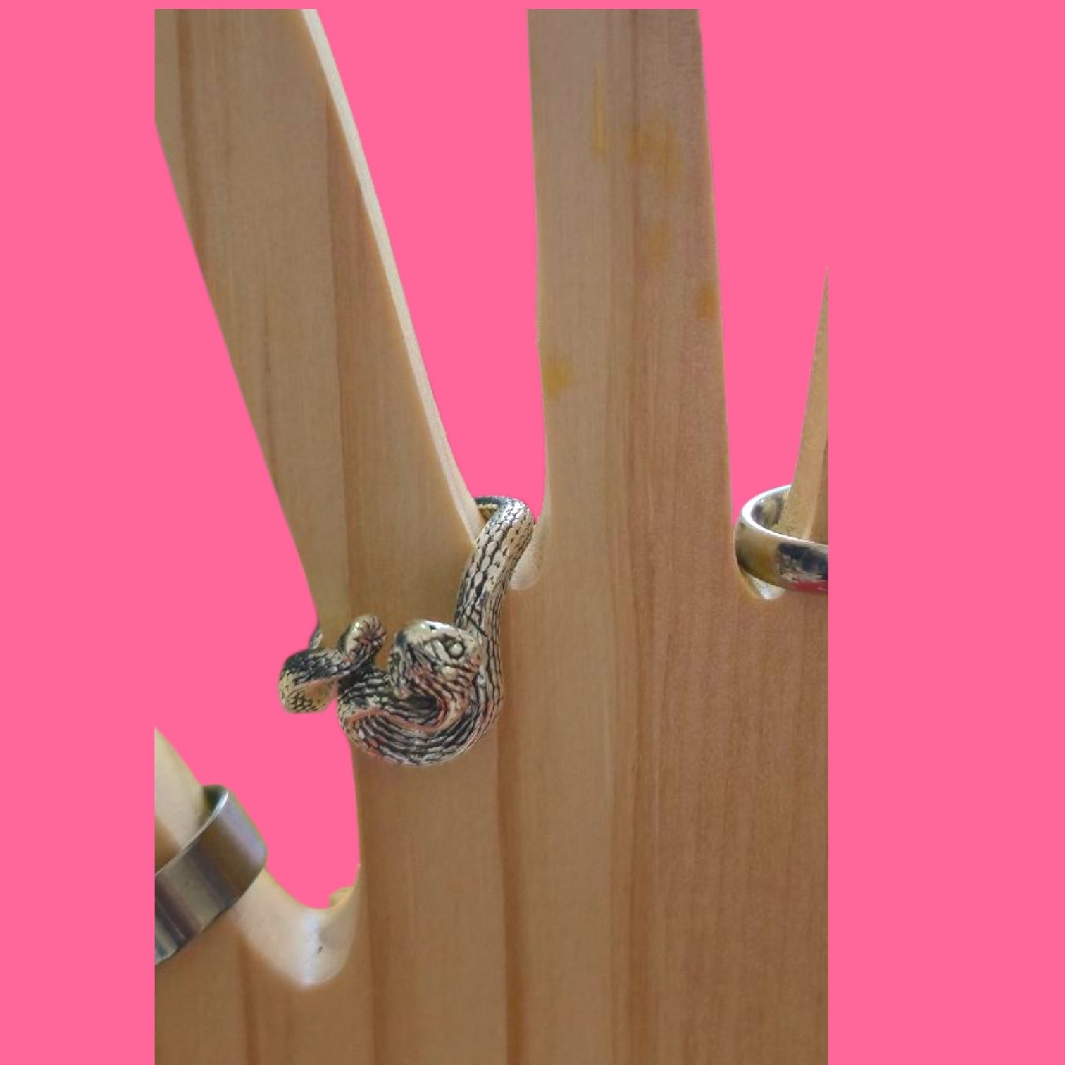 Anillo de perezoso plateado sobre un soporte de madera con forma de mano. Fondo rosa.