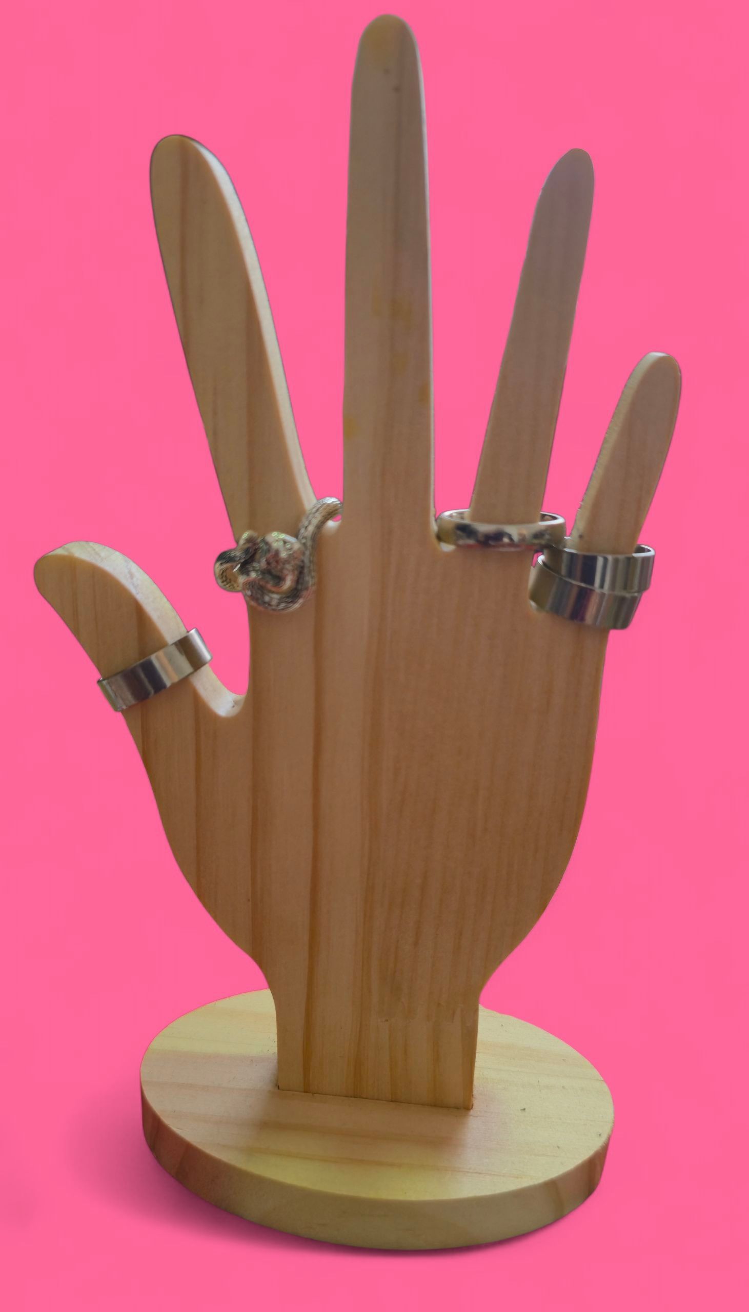 Anillo de perezoso plateado sobre un soporte de madera con forma de mano. Fondo rosa.