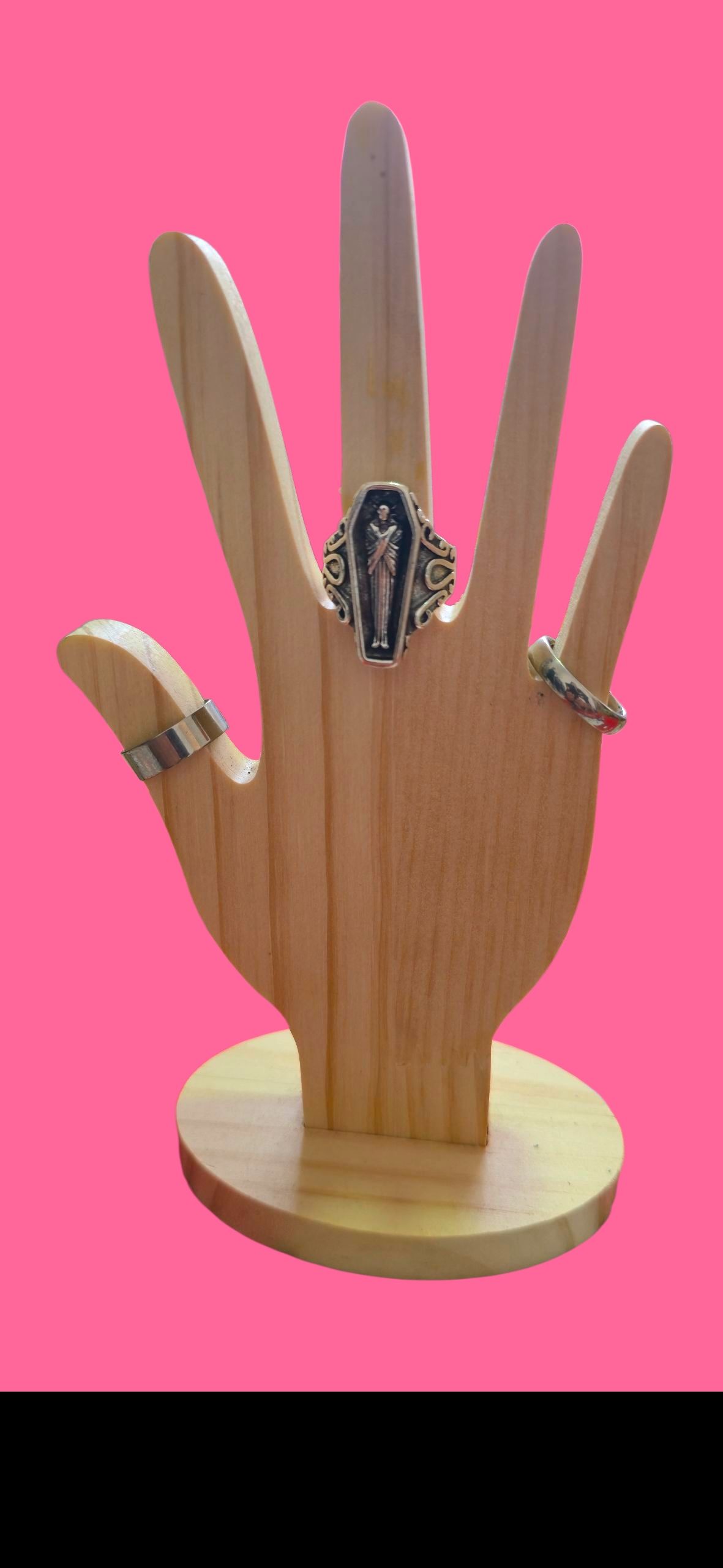 Anillo con diseño de ataúd sobre un soporte de madera con fondo rosa.