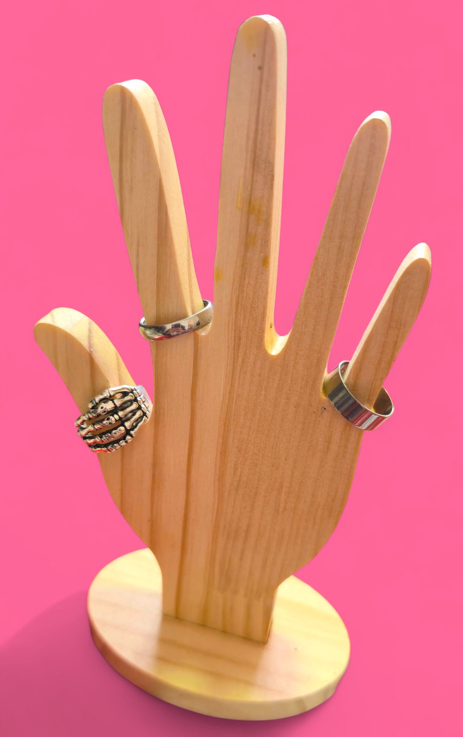 Anillo de plata con forma de mano de esqueleto sobre un soporte de madera, fondo rosa.