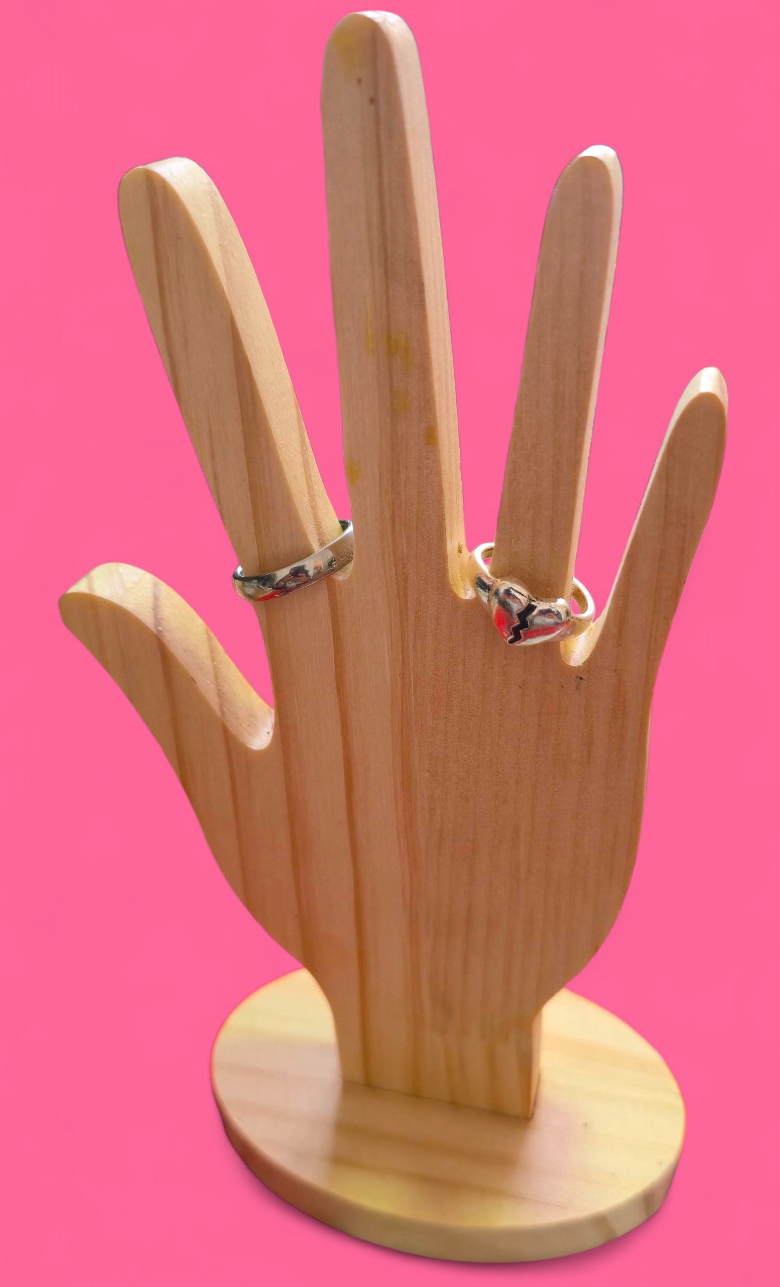 Anillo de plata con un corazón rojo agrietado sobre una mano de madera, sobre un fondo rosa.
