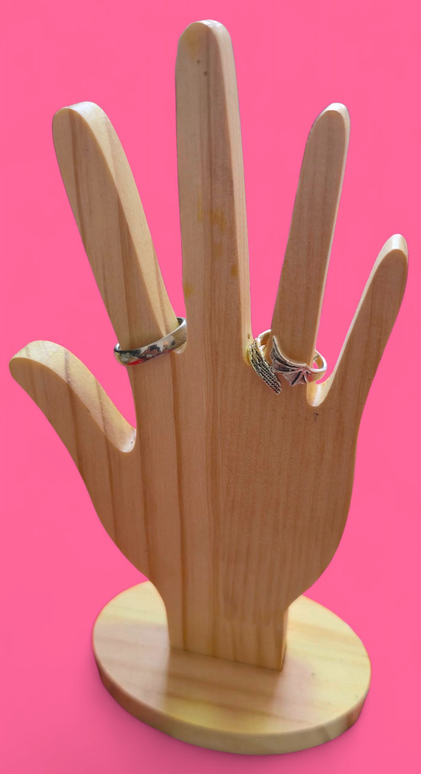 Anillo de plata con diseño de hoja sobre una mano de madera con fondo rosa.