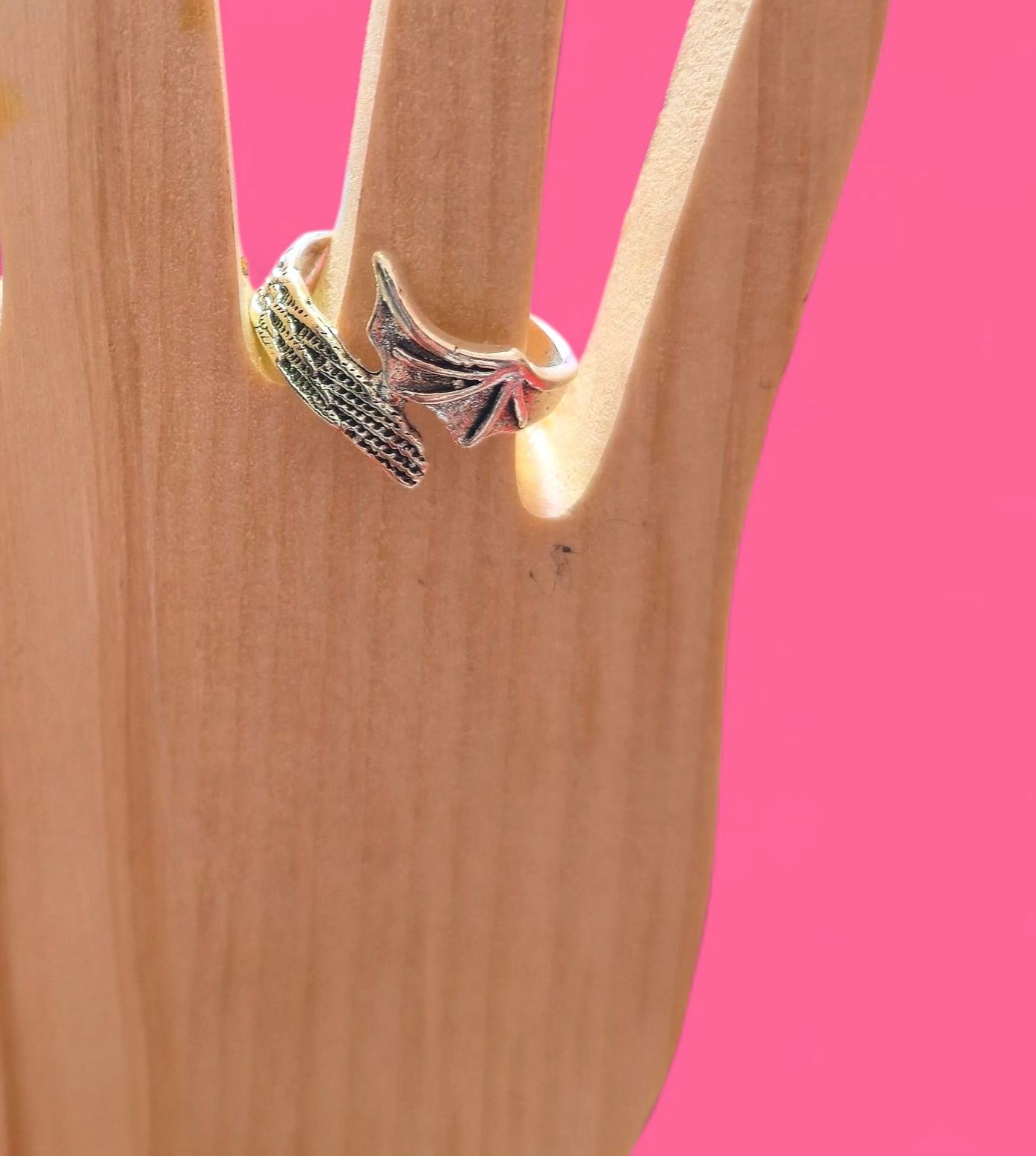 Anillo de plata con diseño de hoja sobre una mano de madera con fondo rosa.