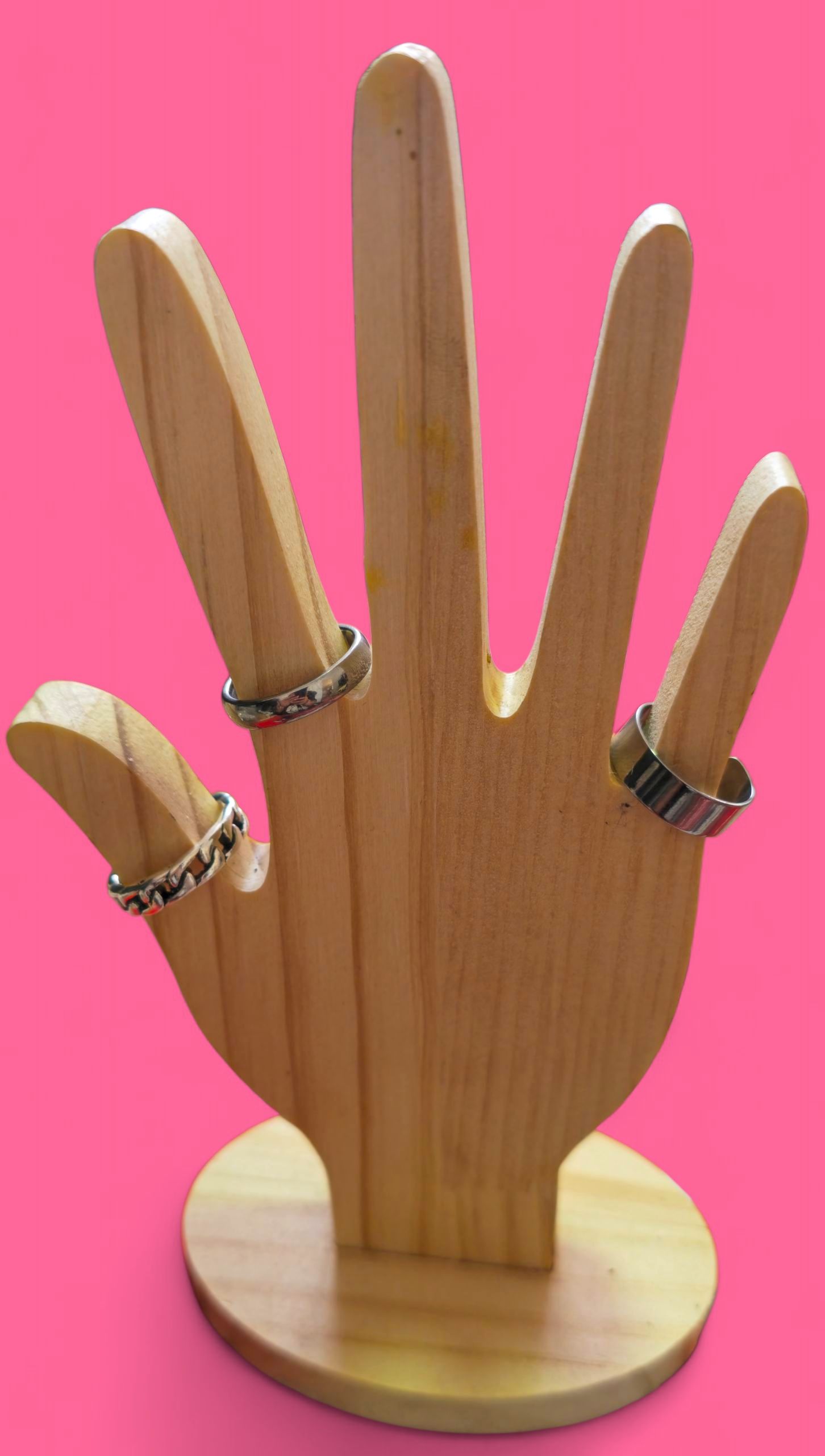 Anillo de cadena plateada sobre una mano de madera contra un fondo rosa brillante.