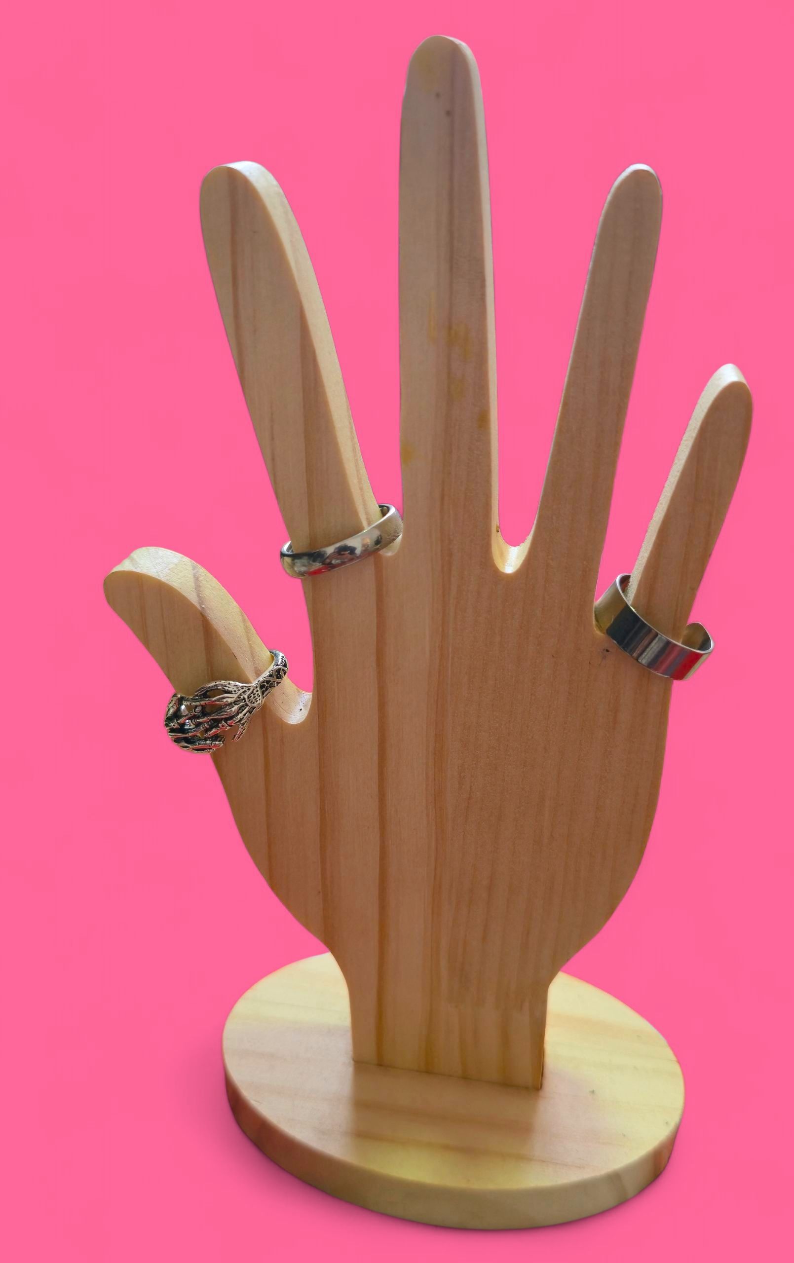 Anillo de plata con forma de mano de esqueleto sobre un soporte de madera, fondo rosa.