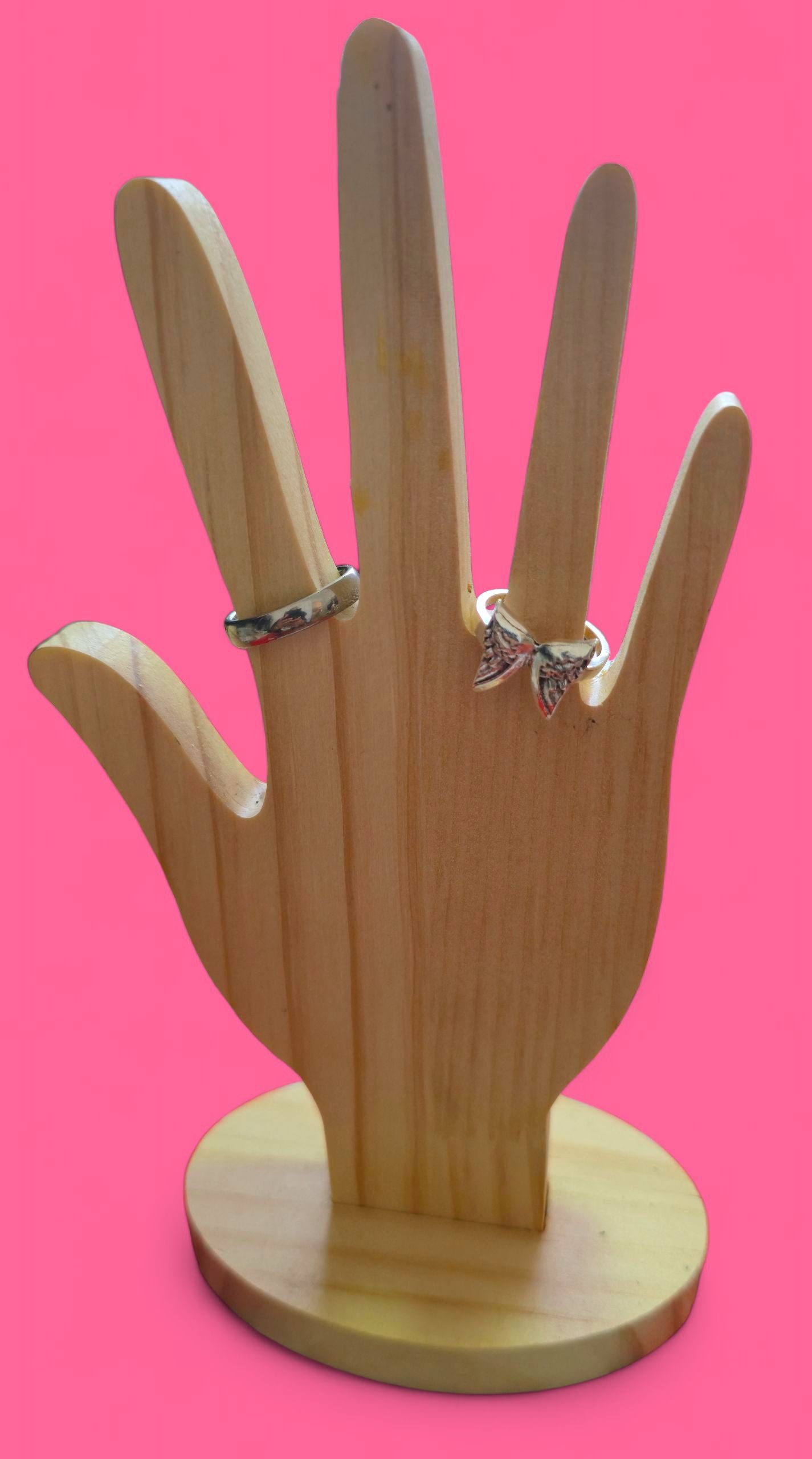 Anillo de lazo plateado en una mano, fondo rosa.