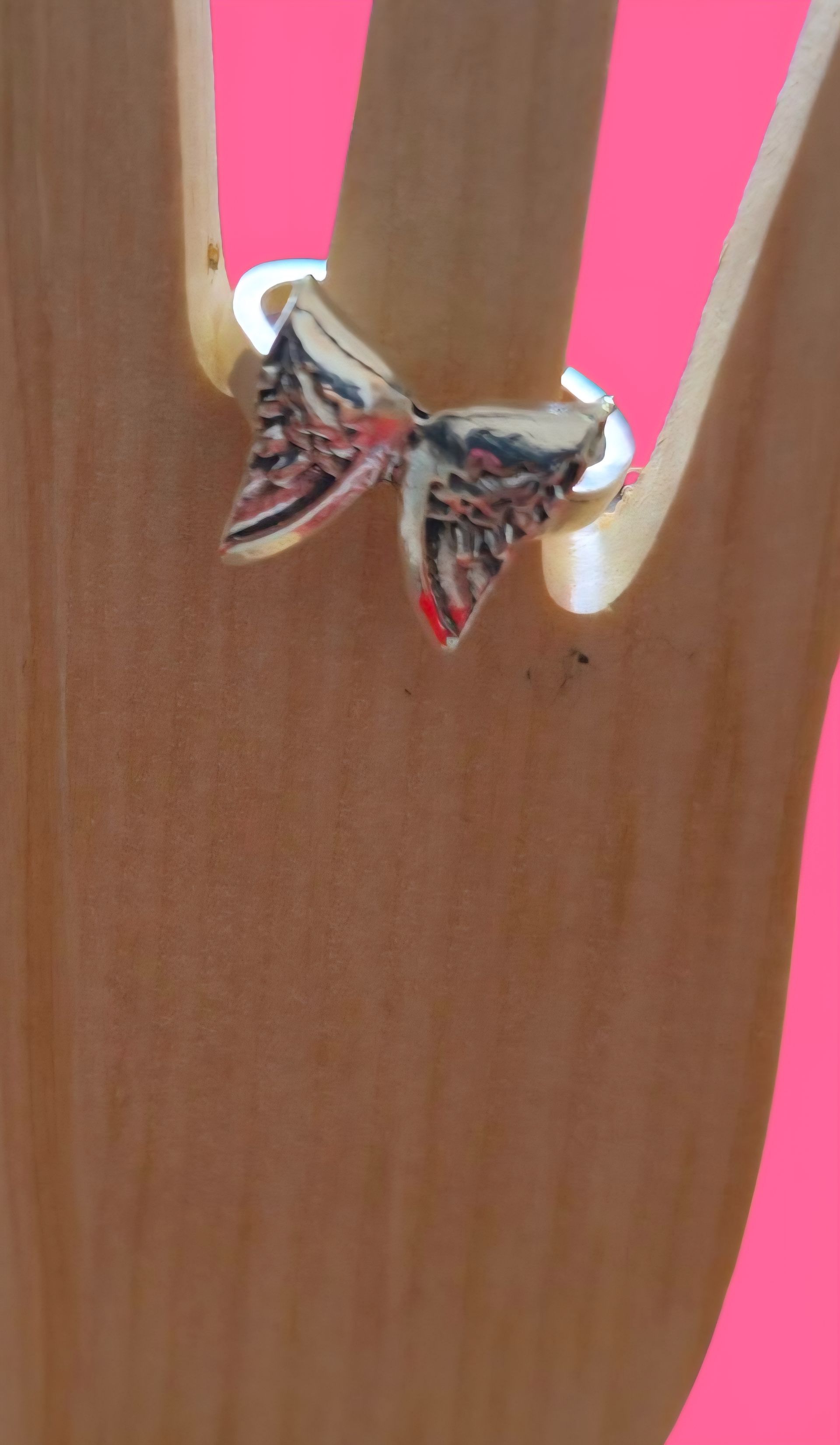 Anillo de lazo plateado en una mano, fondo rosa.