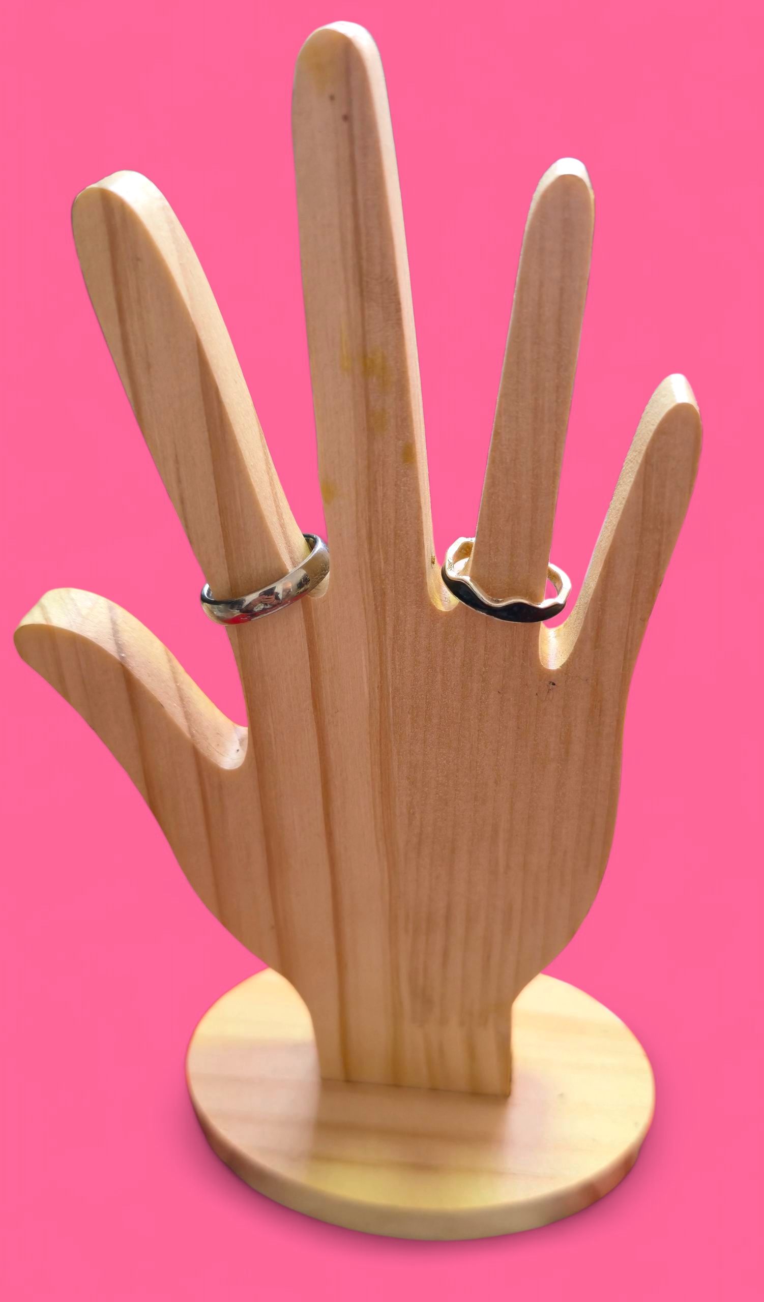Anillo con diseño de ola negra sobre un soporte de madera con forma de mano, sobre un fondo rosa.