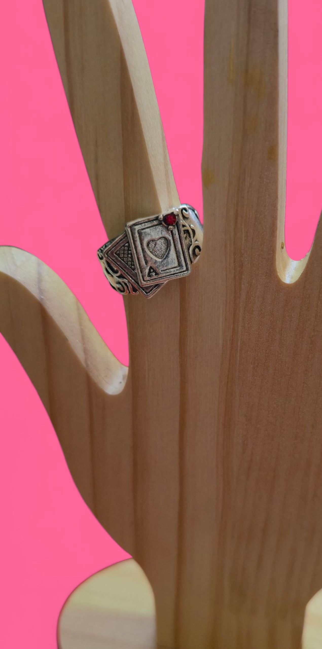 Un anillo con una piedra roja está engastado en una mano de madera sobre un fondo rosa.