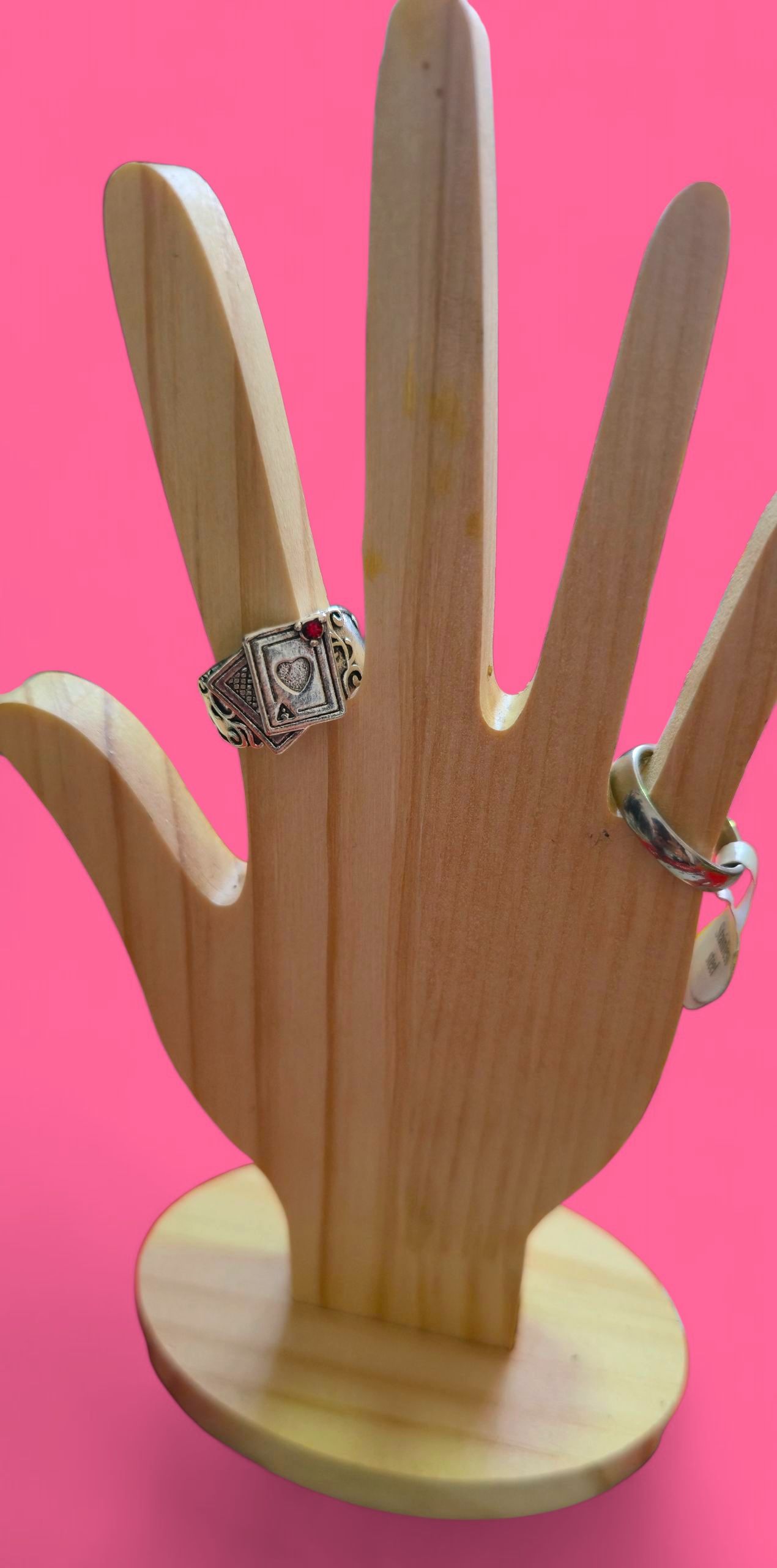 Un anillo con una piedra roja está engastado en una mano de madera sobre un fondo rosa.