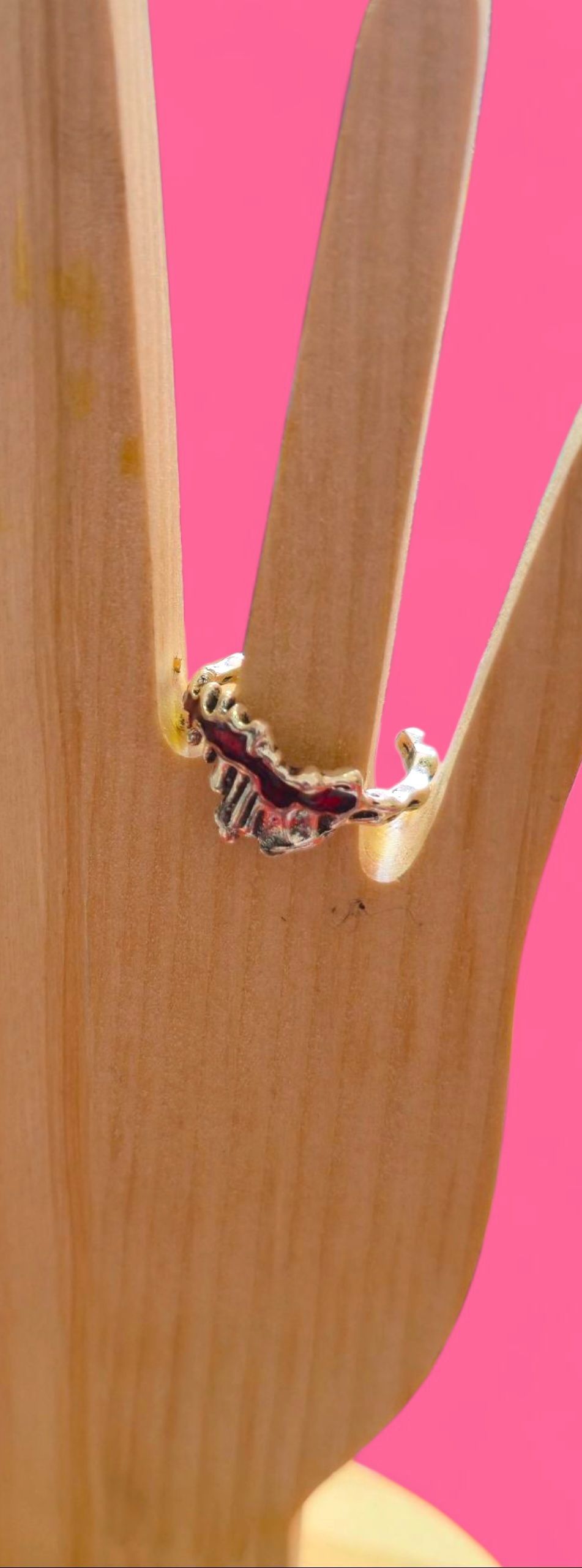 Un anillo de plata con detalles ornamentales descansa sobre una mano de madera contra un fondo rosa.
