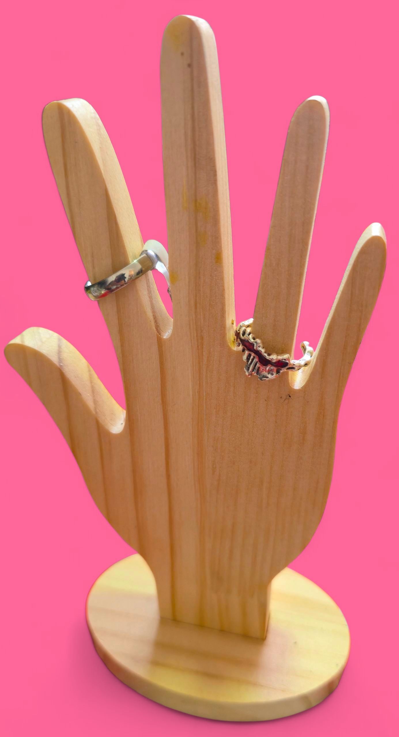 Un anillo de plata con detalles ornamentales descansa sobre una mano de madera contra un fondo rosa.