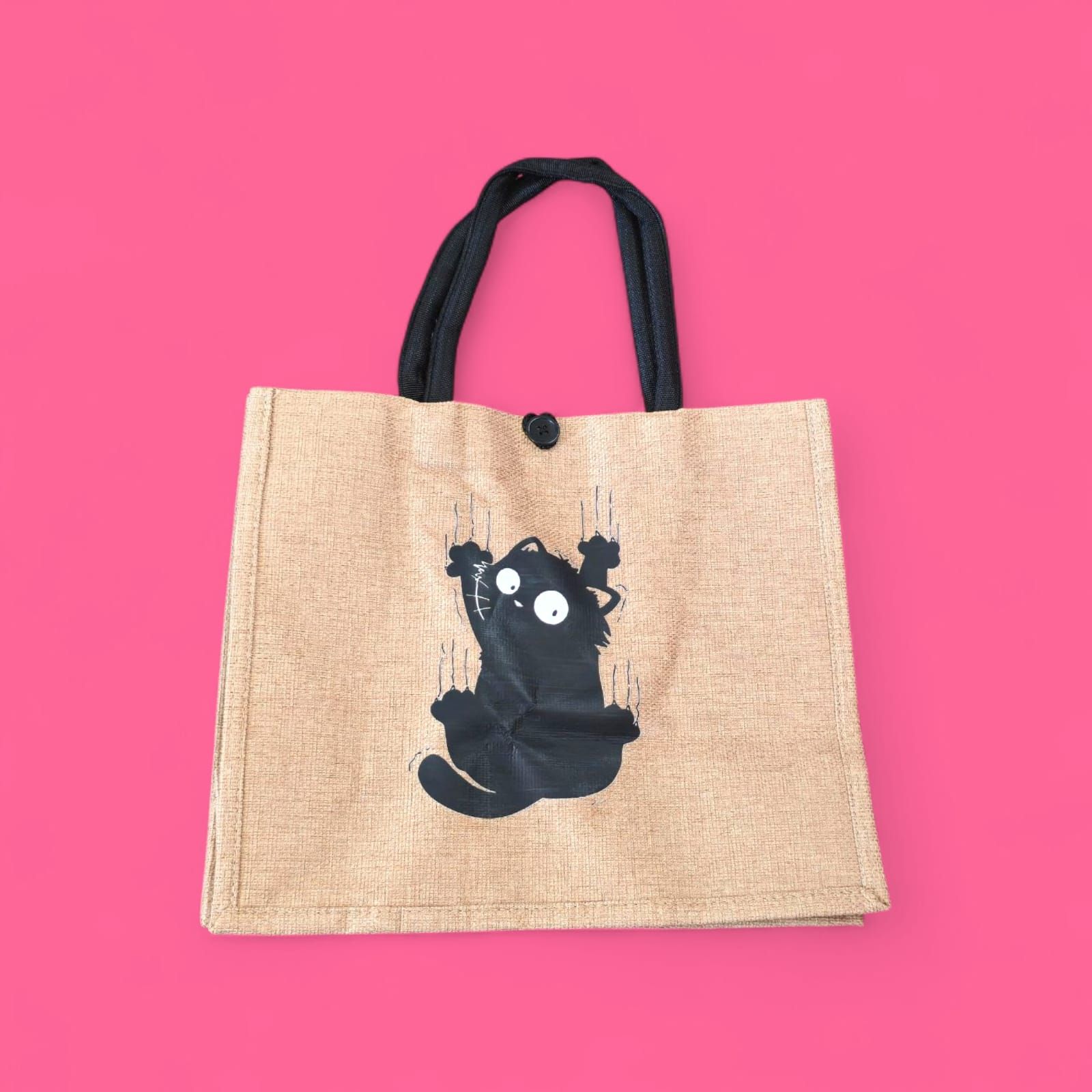 Una persona con chaqueta de cuero negra y vaqueros rotos sostiene un bolso tote con un dibujo de un gato.