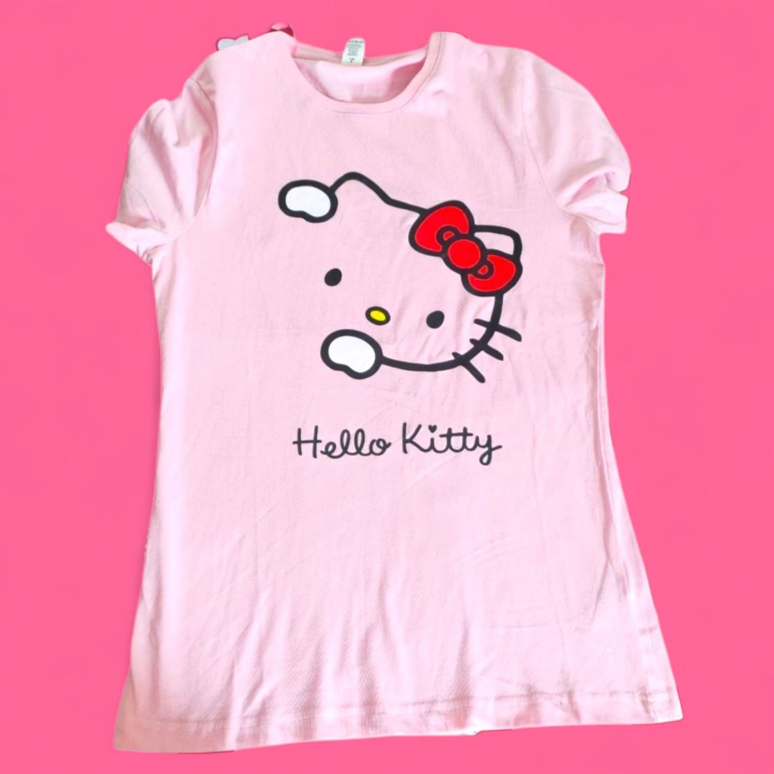 Mujer rapada, vestida con una camiseta rosa de Hello Kitty, vaqueros negros rotos y botas, de pie en un callejón.