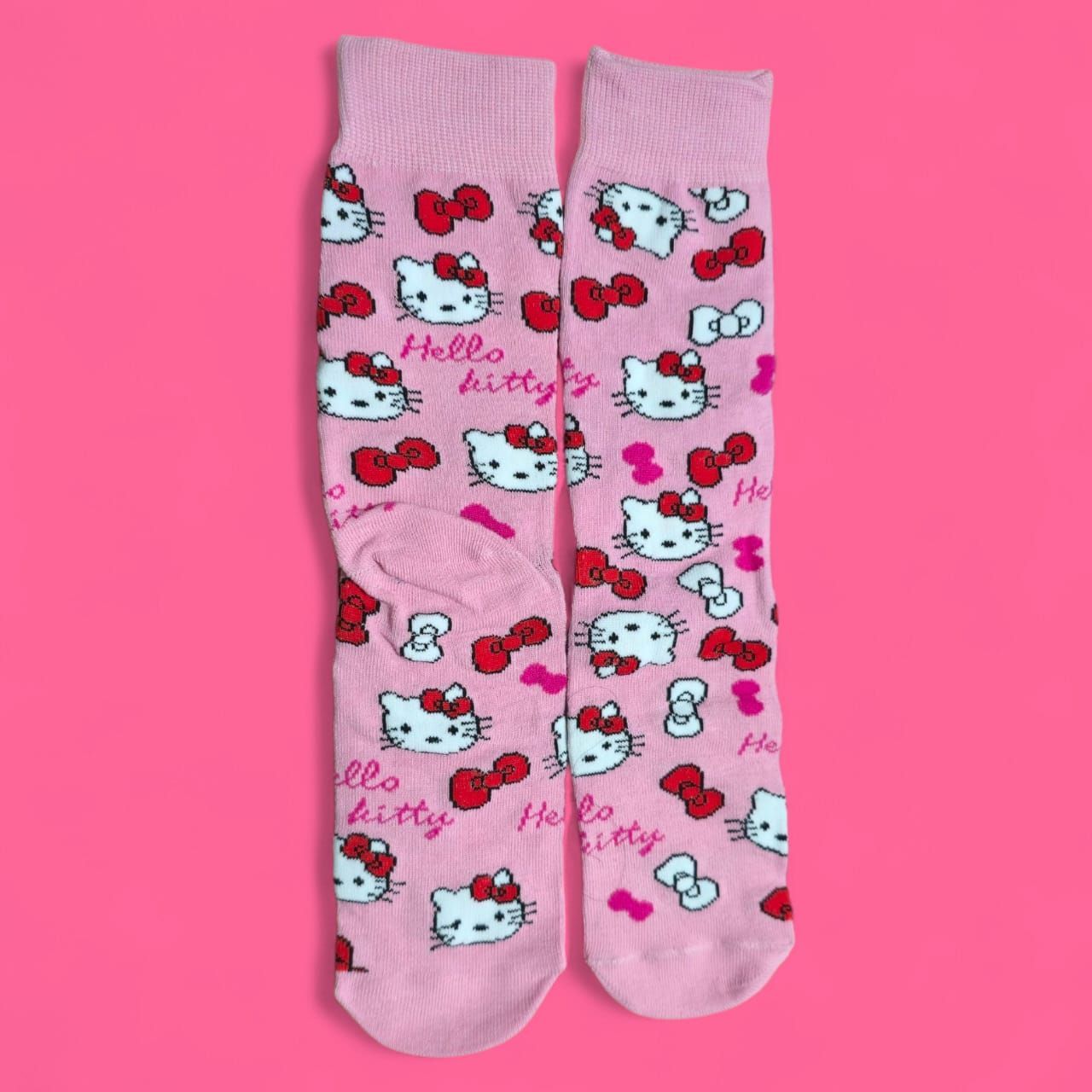 Calcetines rosas de Hello Kitty con lazos rojos, sobre fondo rosa.