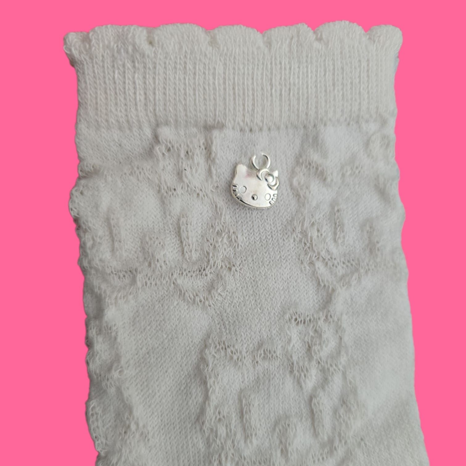 Dos calcetines de encaje color crudo con borde festoneado y un pequeño detalle de cuentas plateadas, sobre un fondo rosa.