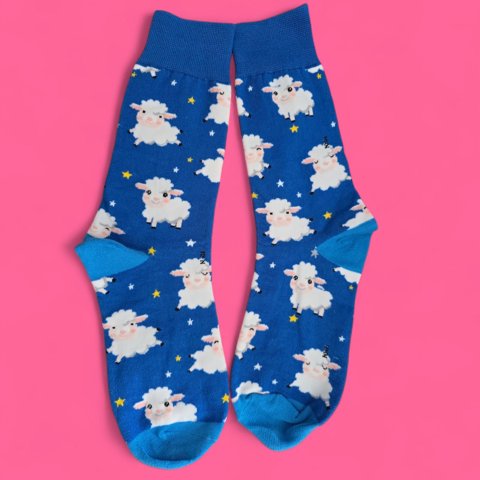Calcetines azules con ovejas blancas y estrellas amarillas sobre fondo rosa.