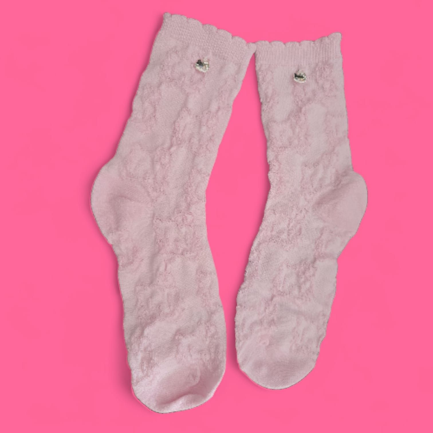 Dos calcetines de encaje rosa claro sobre fondo rosa, con pequeños adornos decorativos.