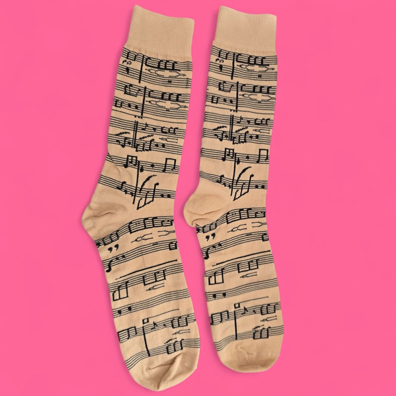 Un par de calcetines color canela estampados con notas musicales negras, sobre una superficie rosa.
